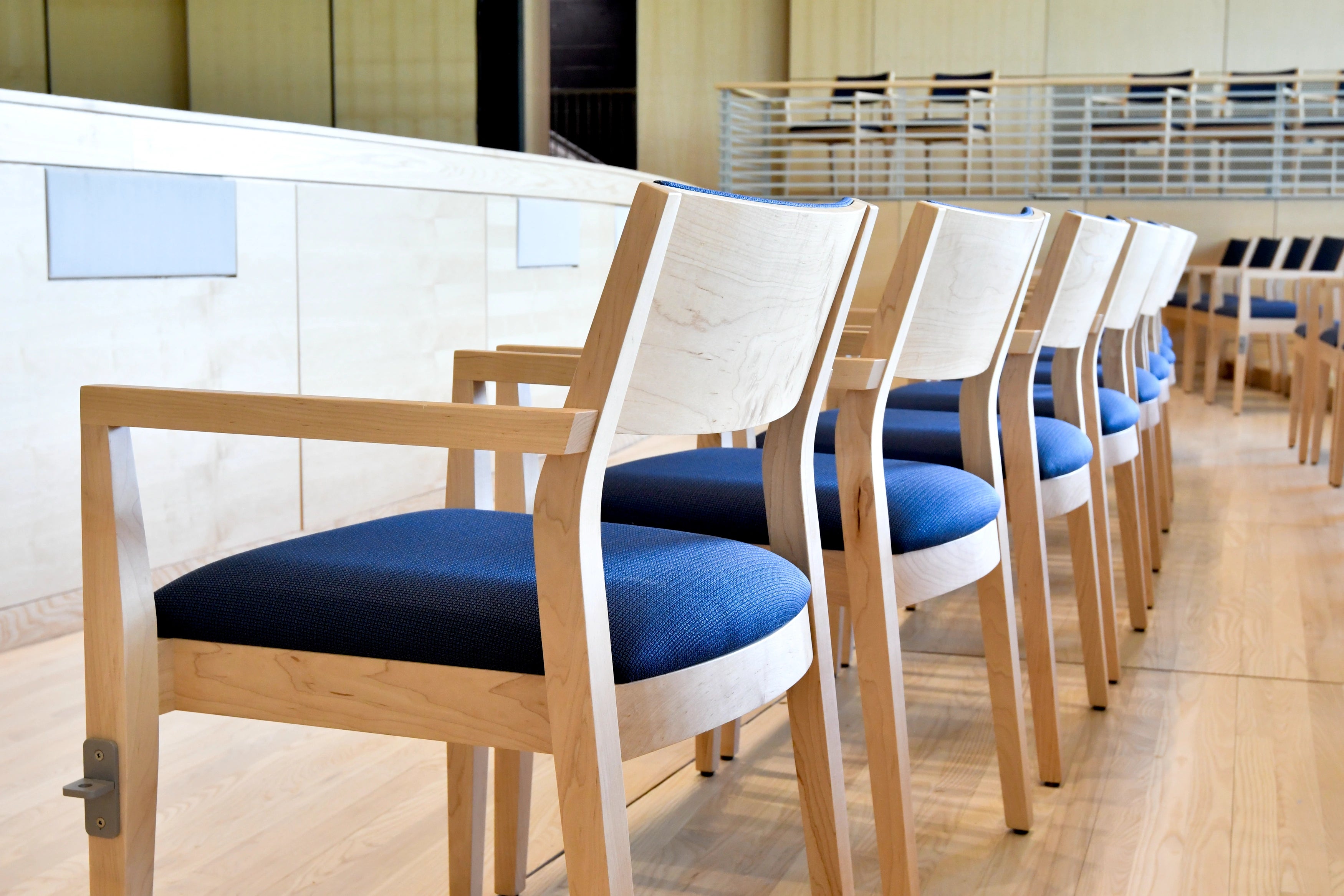 Row of wooden chairs with blue cushions in a room with large windows.