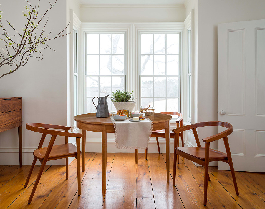 Smaller dining room table with three chairs in front of large window.