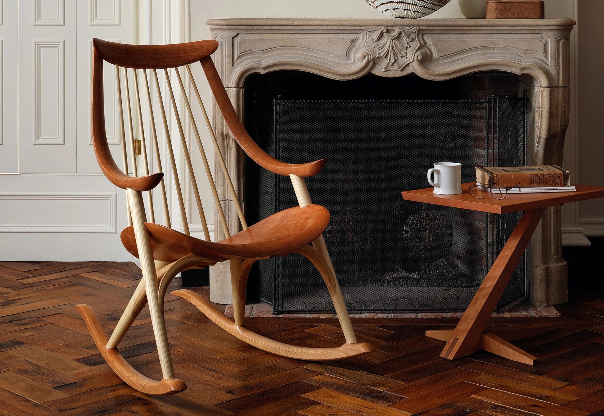 Wooden rocking chair in front of a fireplace with a side table.