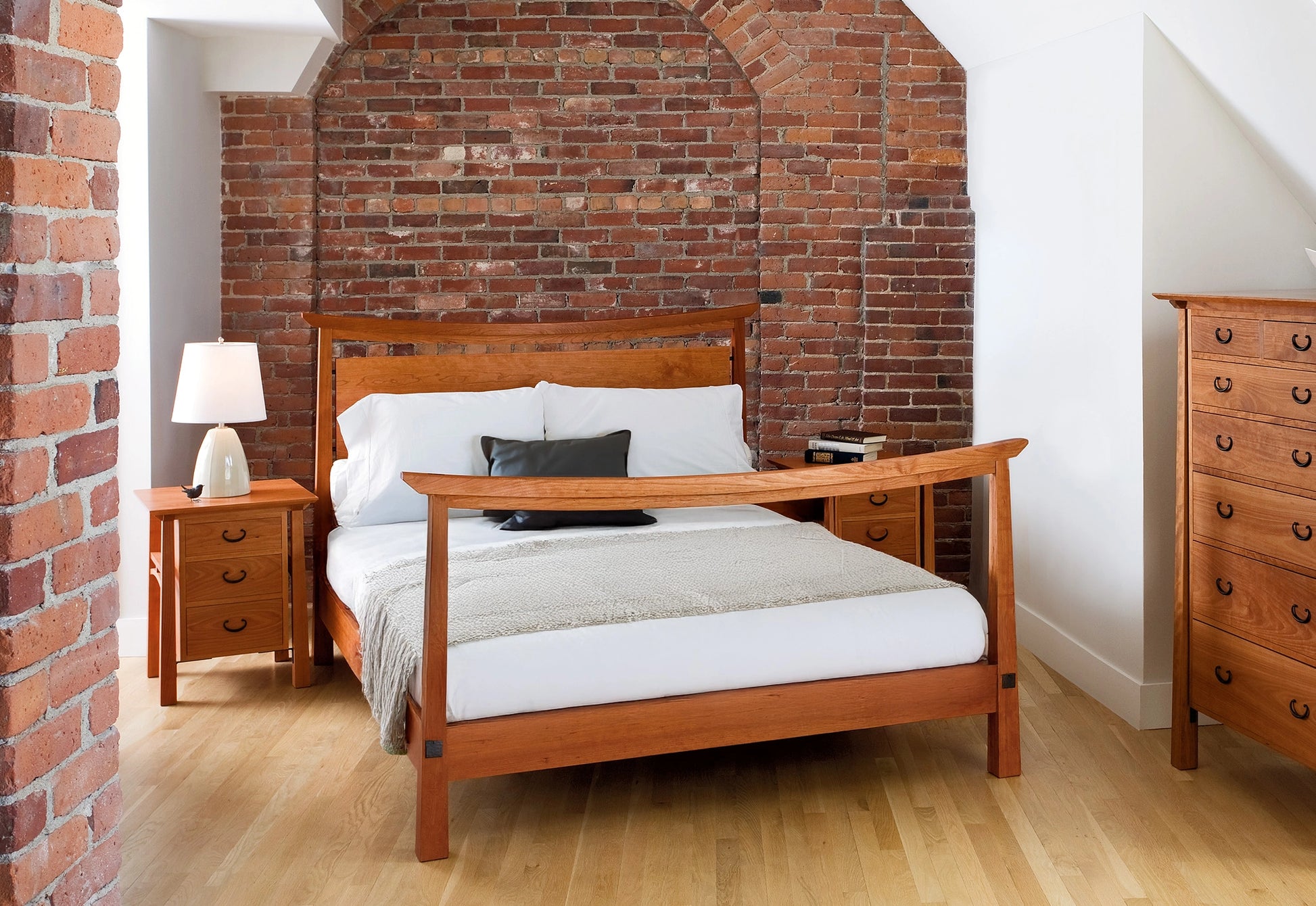 Wooden bed with white bedding against a brick wall in a bedroom setting.