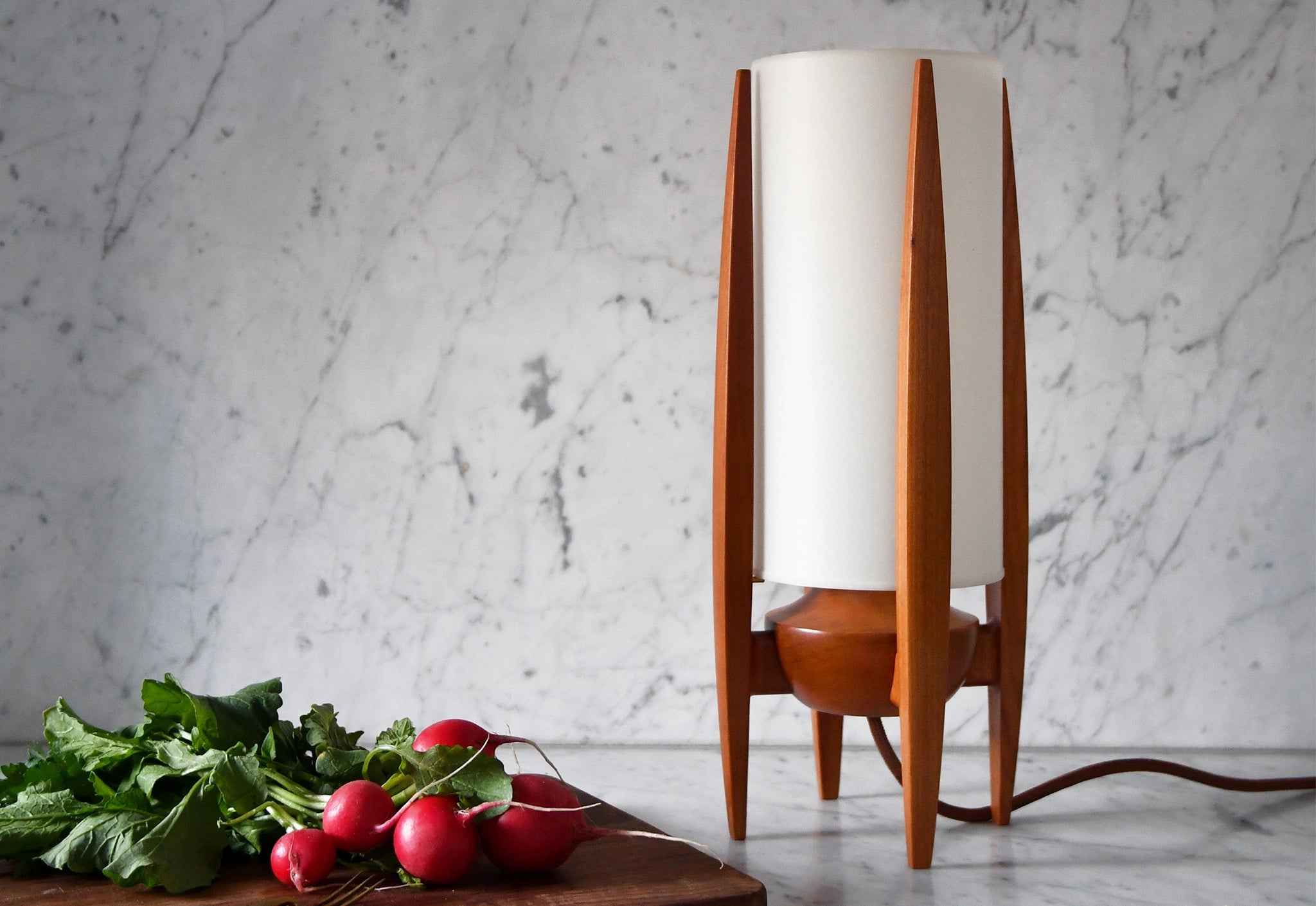 Wooden table lamp with a white shade on a marble surface next to radishes.