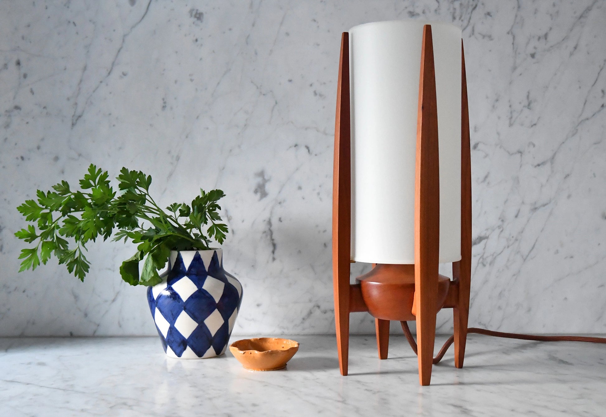 Wooden table lamp with white shade next to a plant and decorative bowl on a marble surface.