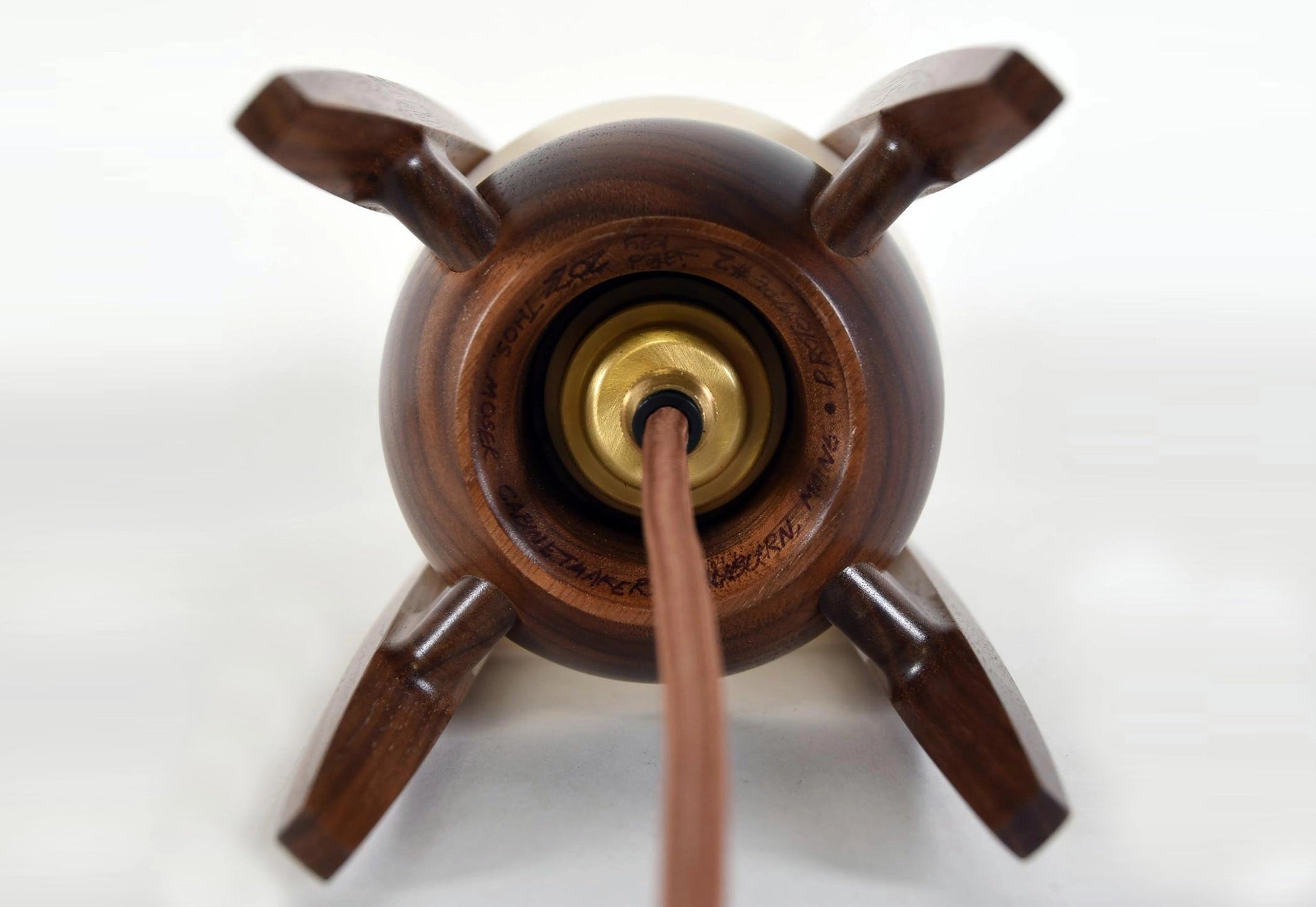 Bottom of wooden lamp cord entry with a central brass component on a white background