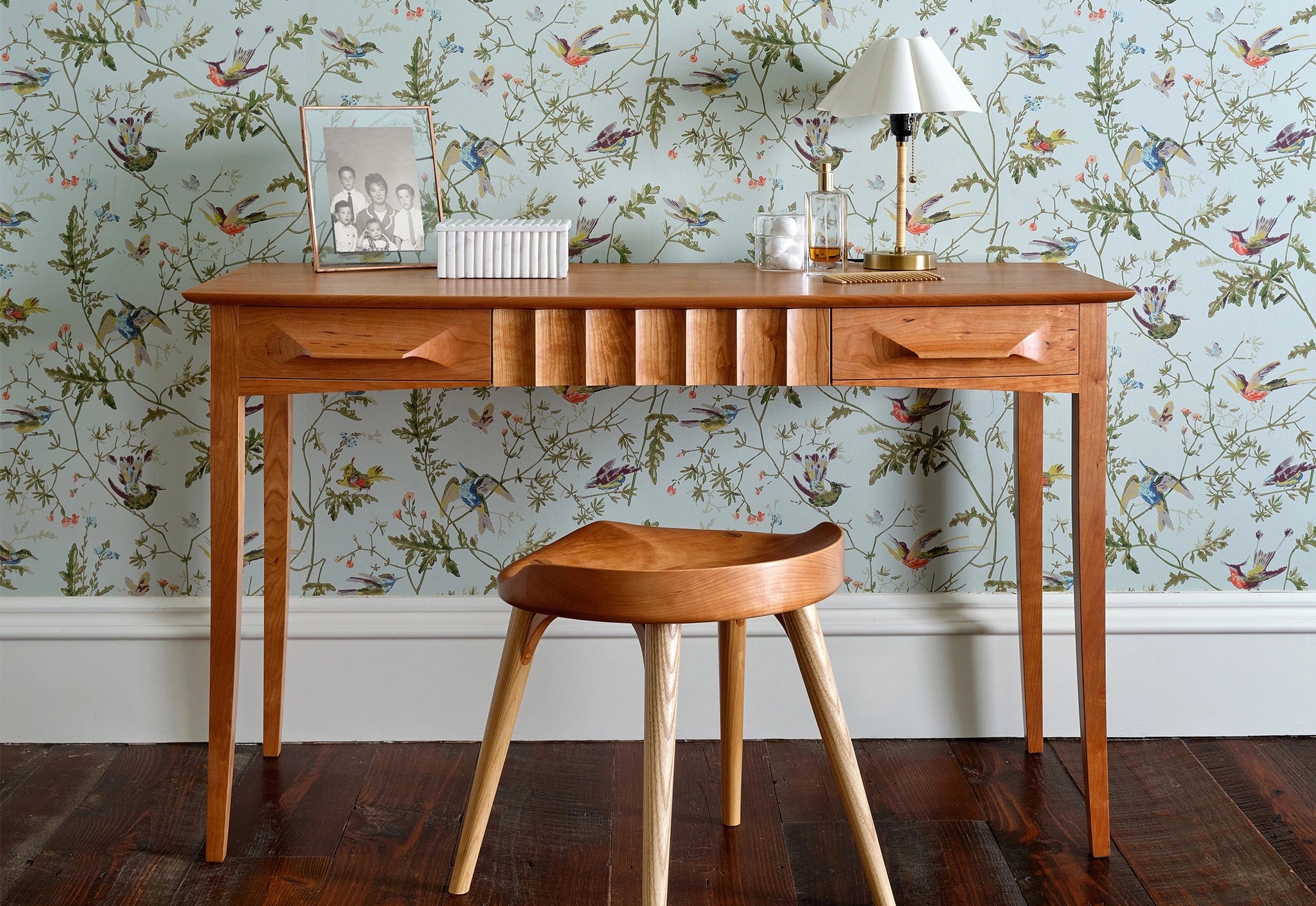 Wooden desk with a chair against a floral wallpapered wall