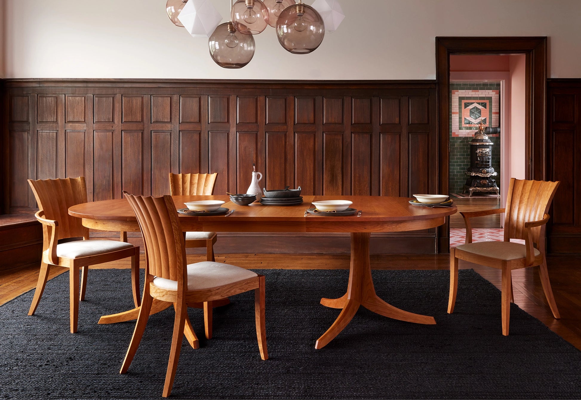 Dining room with wooden table and chairs against a wooden paneled wall.