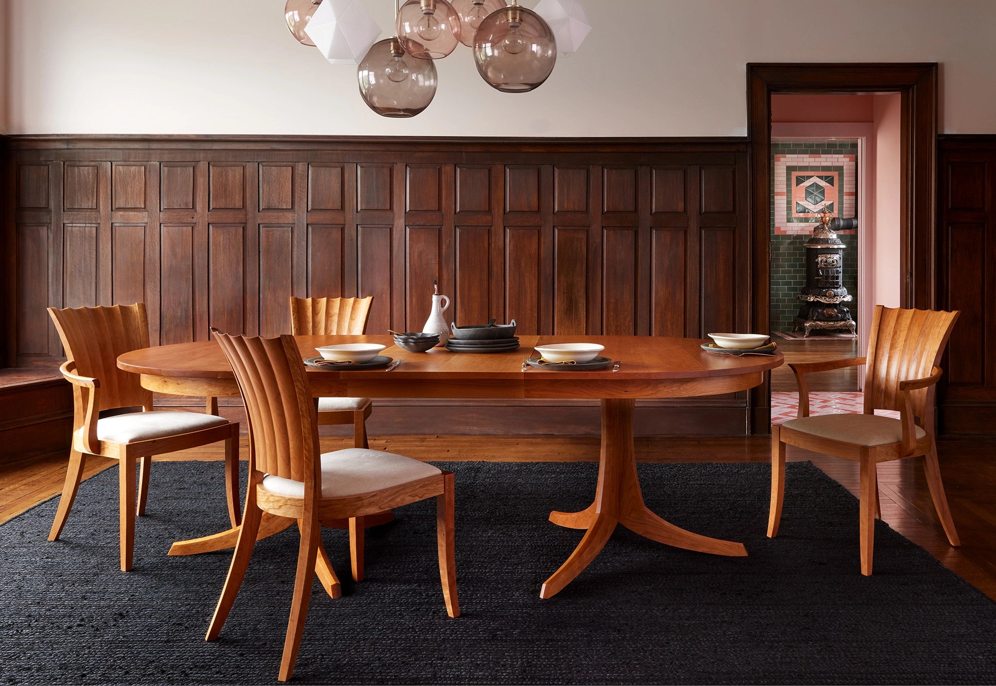 Dining room with wooden table and chairs against a wooden paneled wall.