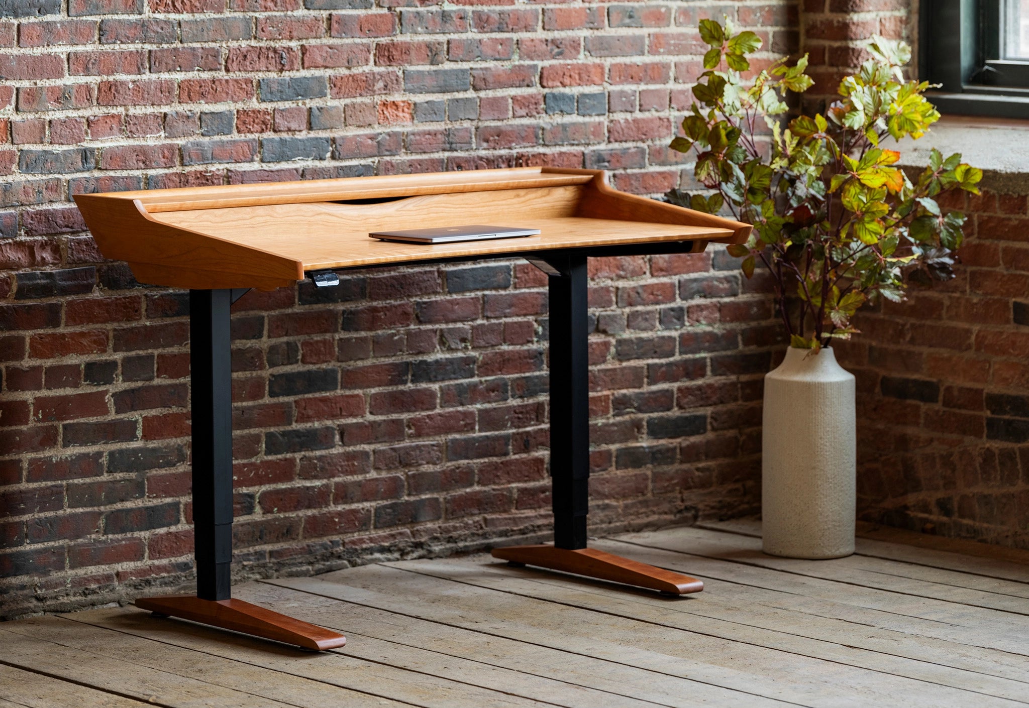 Wooden desk with black legs against a brick wall