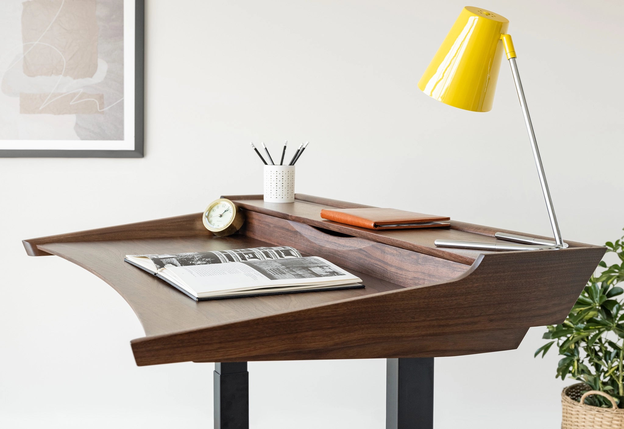 Wooden desk with a yellow lamp, magazine, and office supplies in a home office setting.