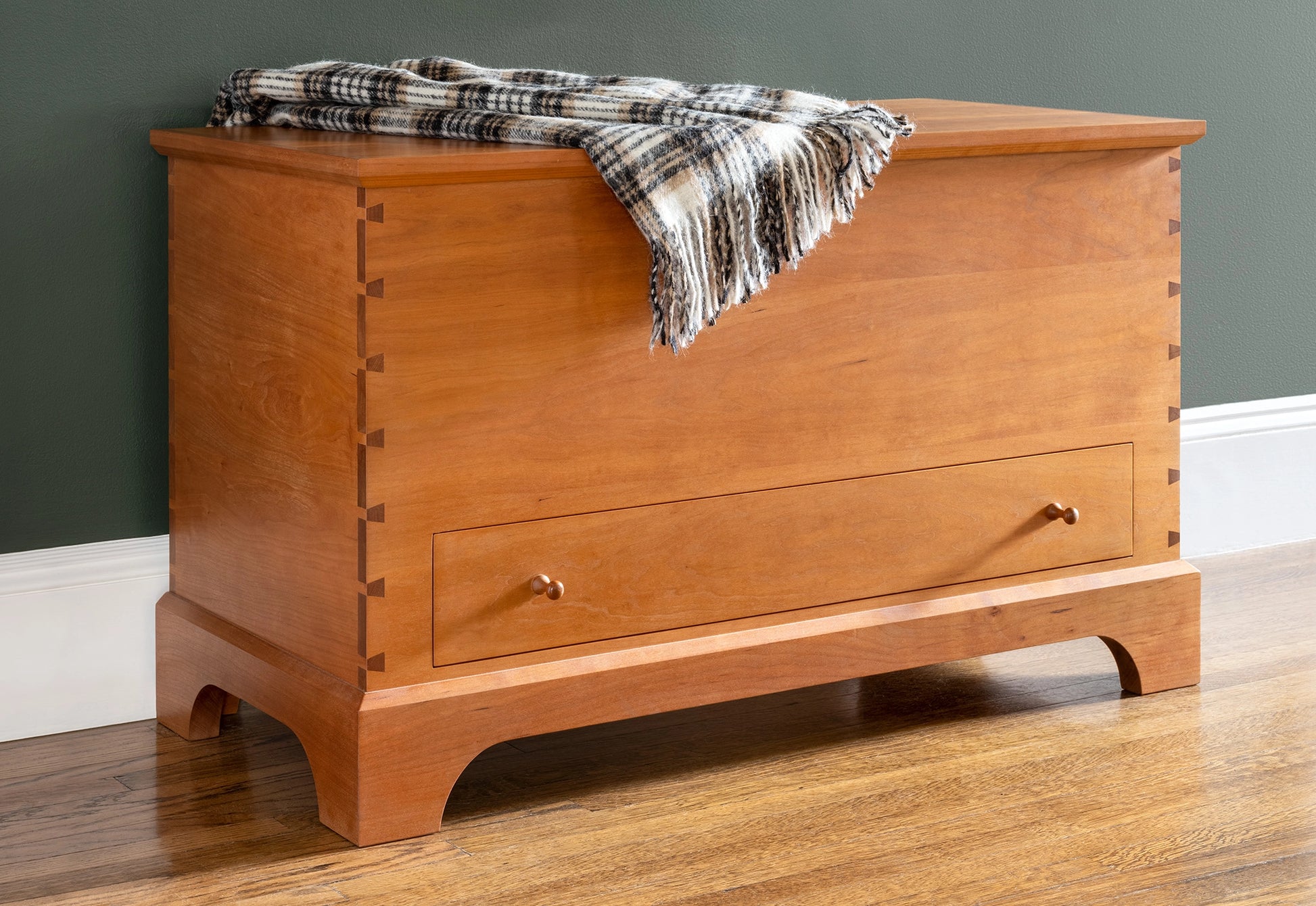 Wooden chest with a plaid blanket on top against a gray wall.