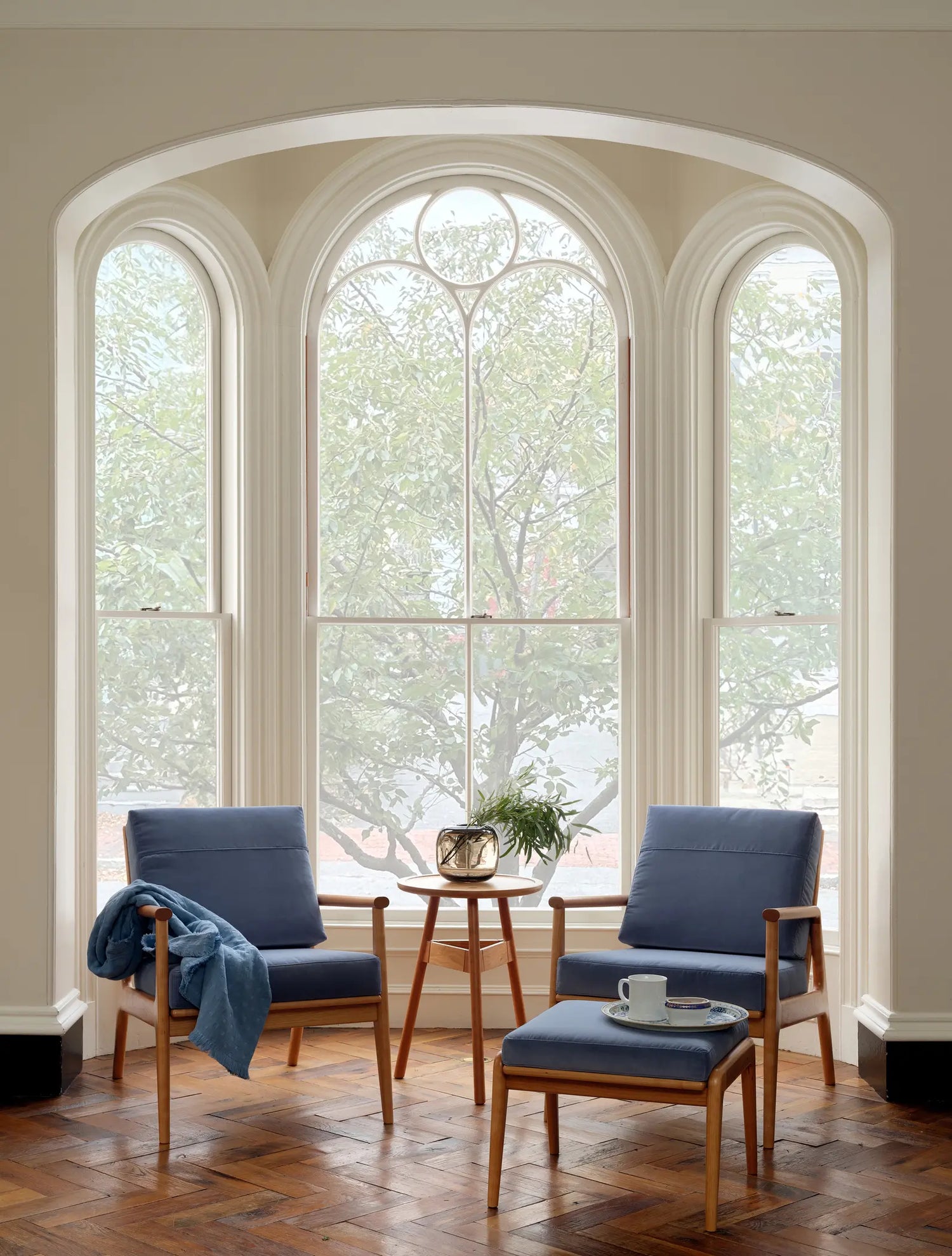 Living room with blue chairs and a coffee table in front of large arched windows.