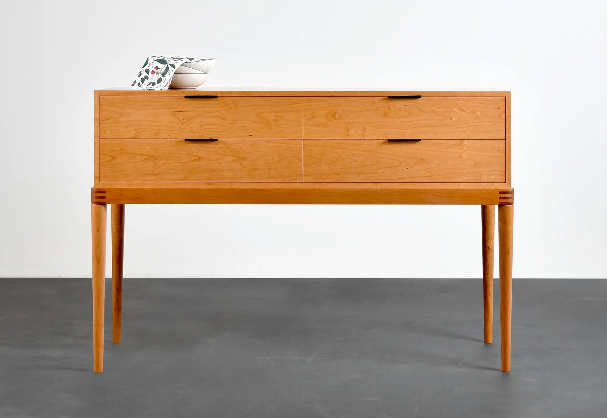 Wooden sideboard with three drawers on a gray floor and white wall background