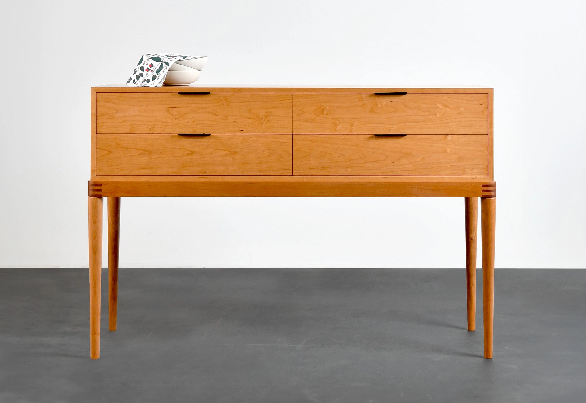 Wooden sideboard with three drawers on a gray floor and white wall background