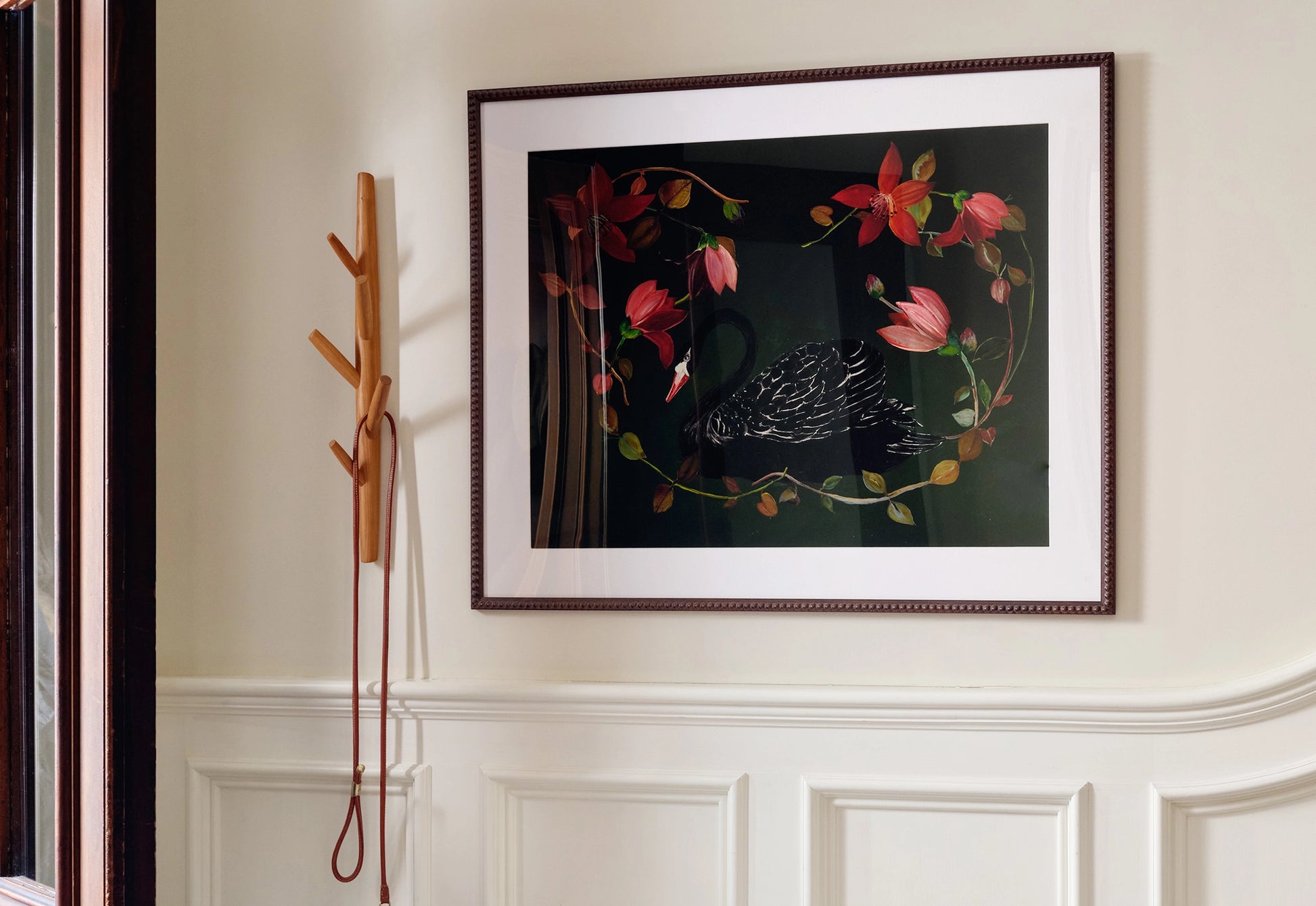 Framed artwork of a bird and flowers on a wall with a wooden coat rack.