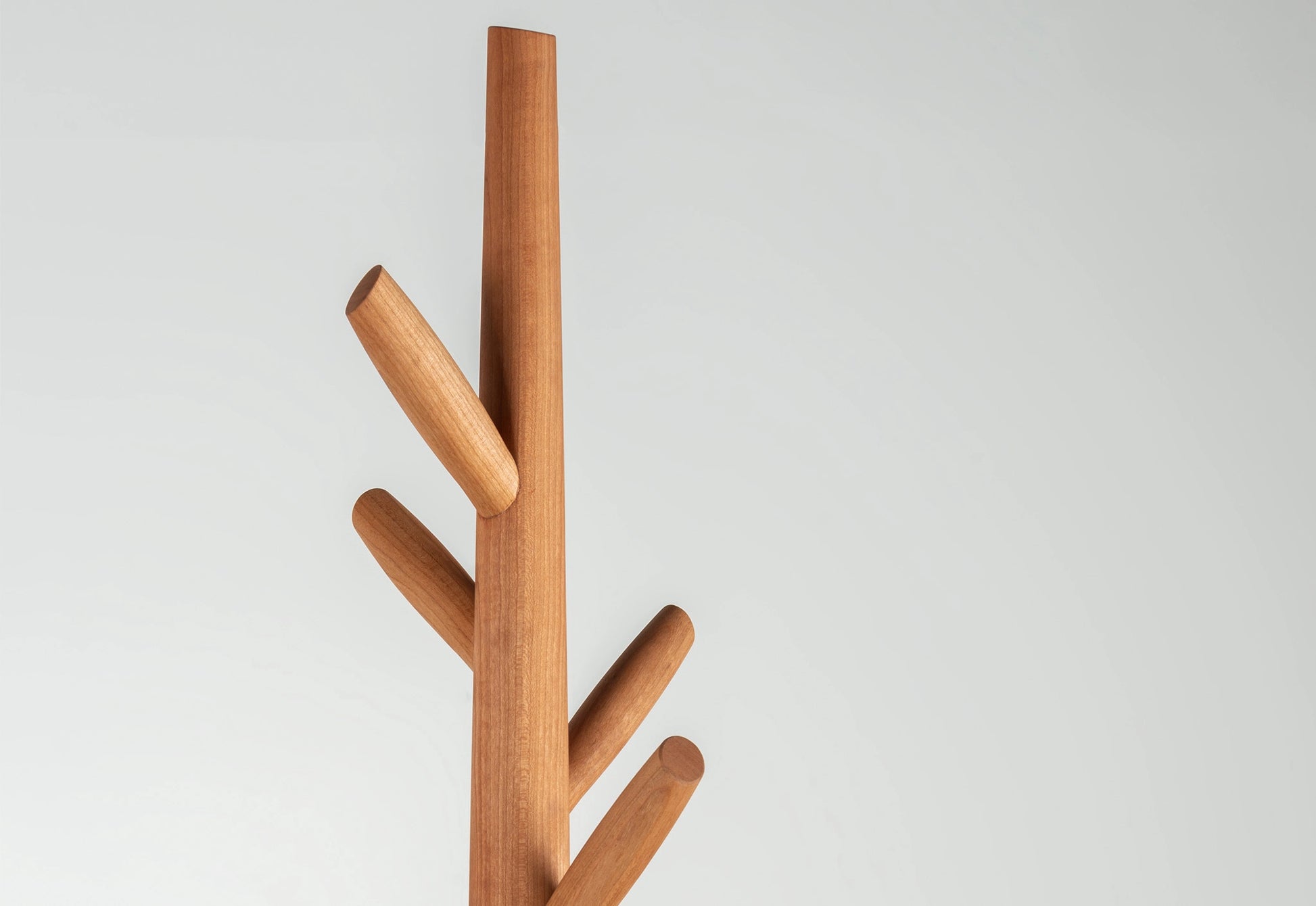Detail of a wooden coat tree with multiple hooks on a light gray background