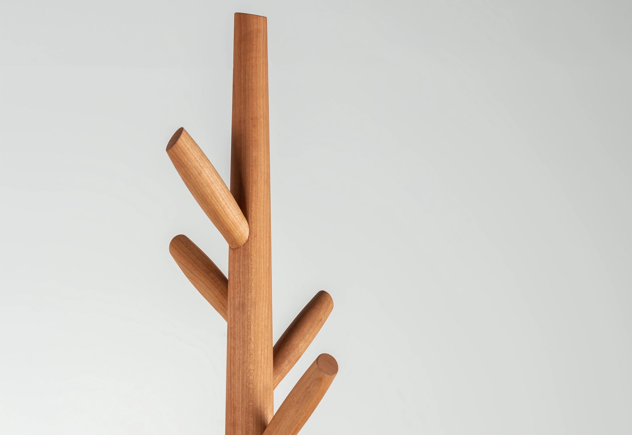 Detail of a wooden coat tree with multiple hooks on a light gray background