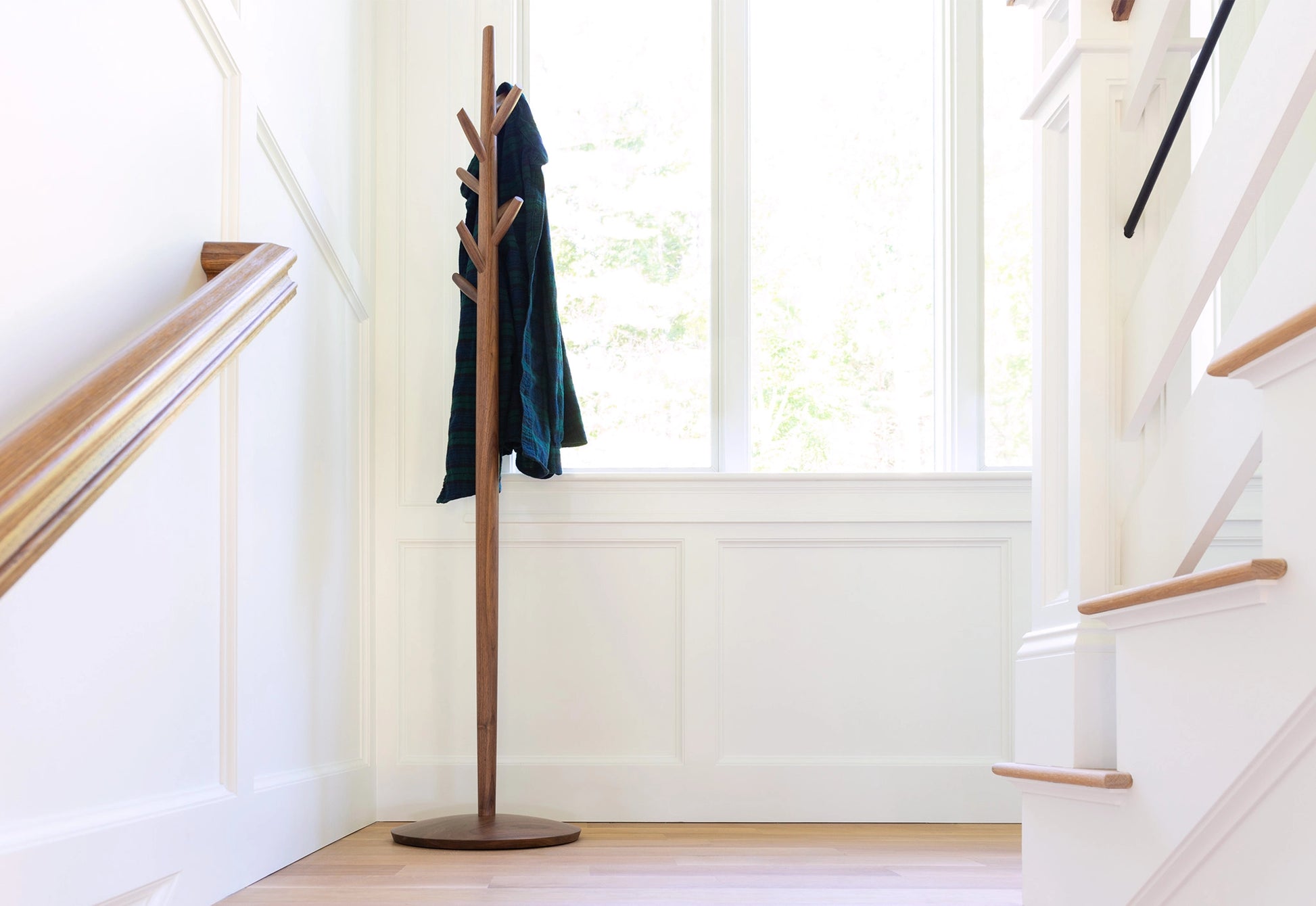Wooden coat tree with a dark jacket in a bright room with a staircase.