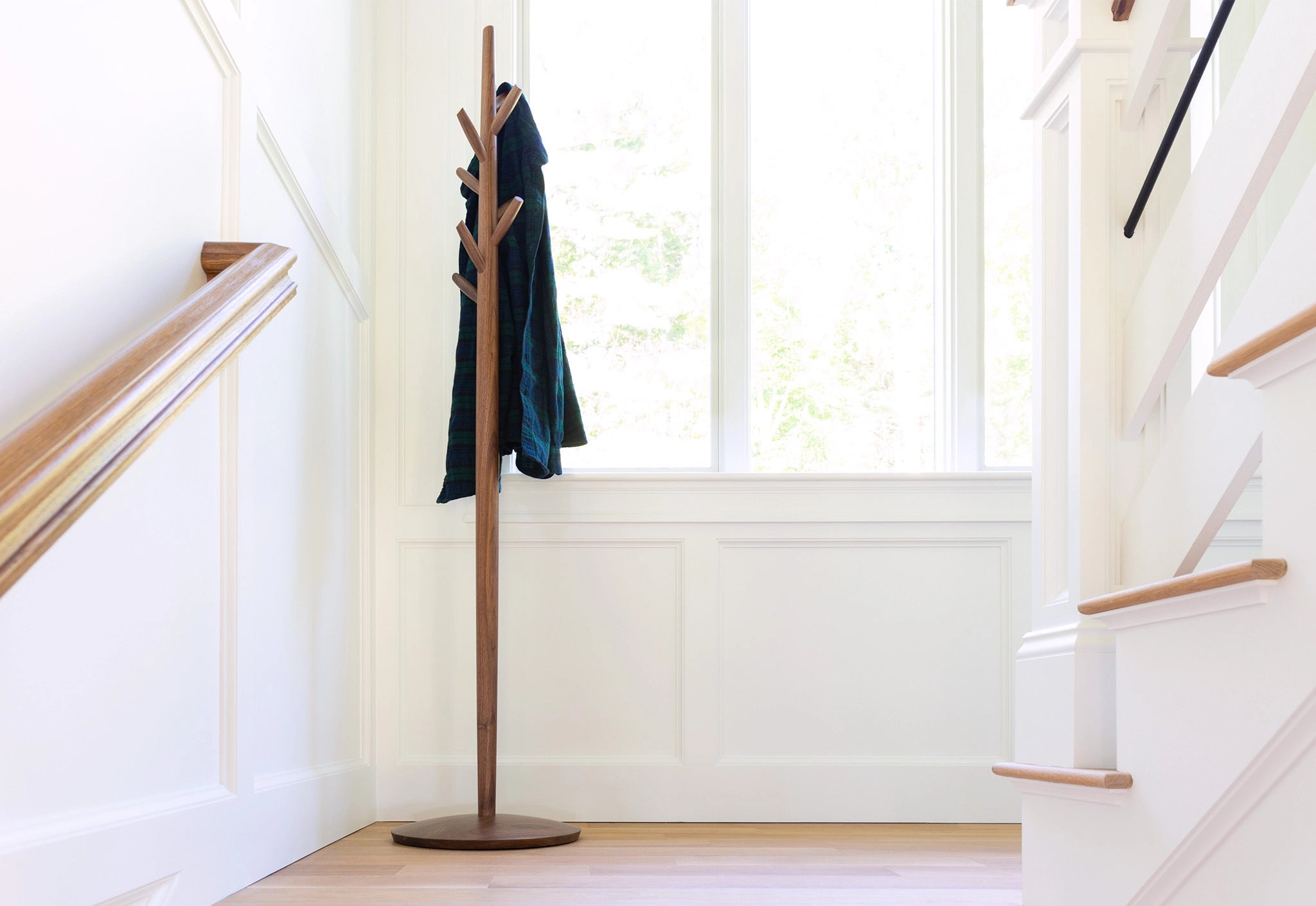 Wooden coat tree with a dark jacket in a bright room with a staircase.