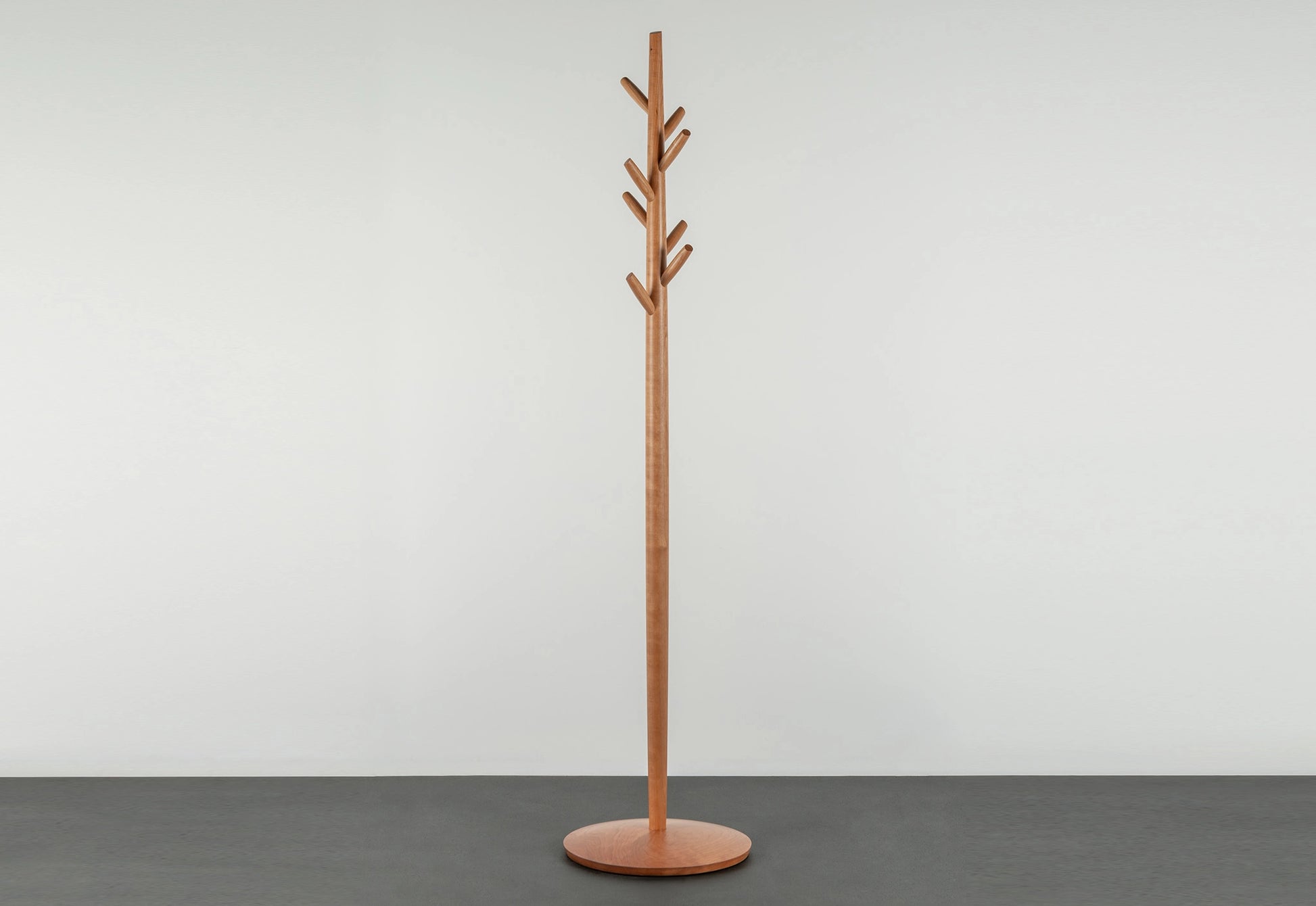 Wooden coat tree with multiple hooks on a gray floor against a white wall