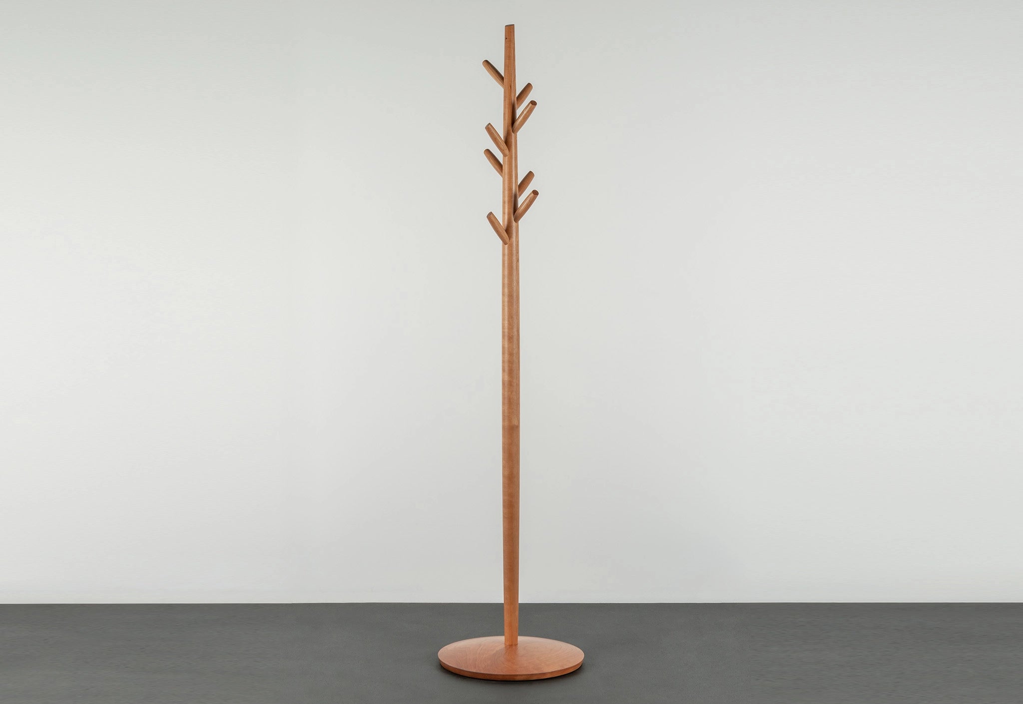 Wooden coat tree with multiple hooks on a gray floor against a white wall