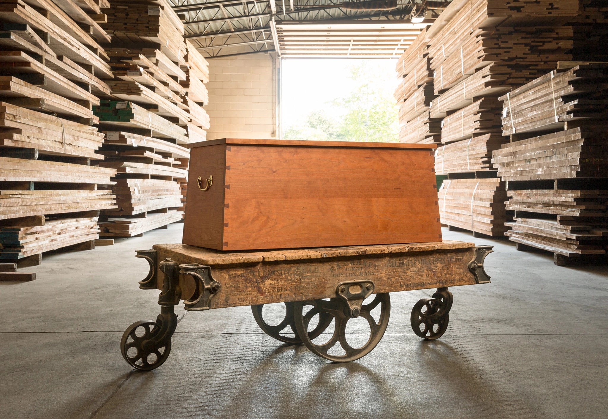 Wooden chest on wheels in a warehouse setting with stacked wooden planks.