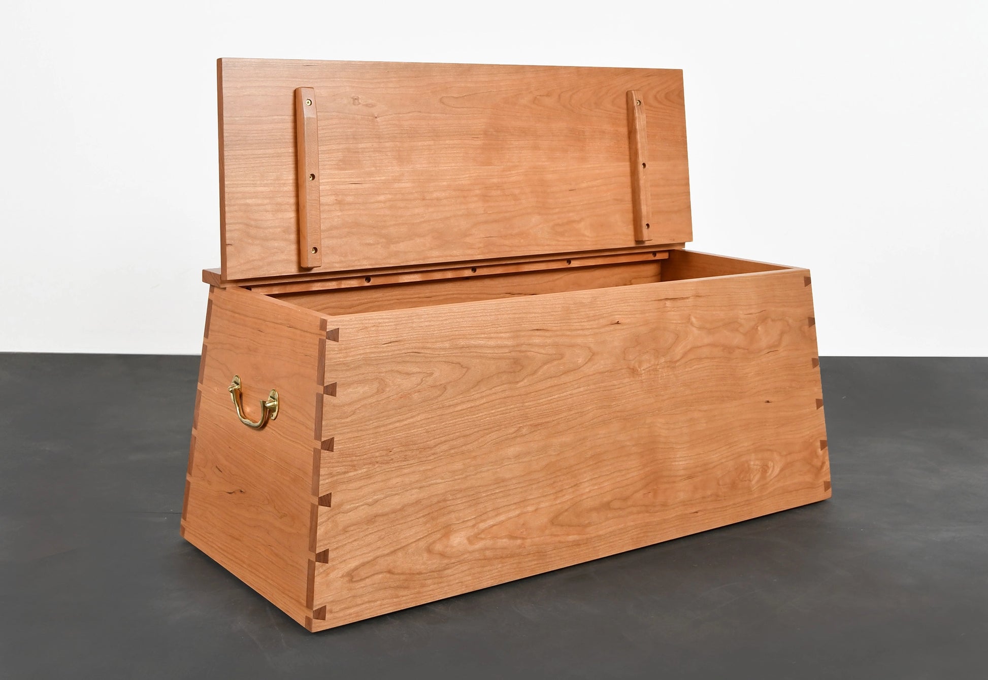 Wooden storage chest with open lid on a dark floor and white wall background