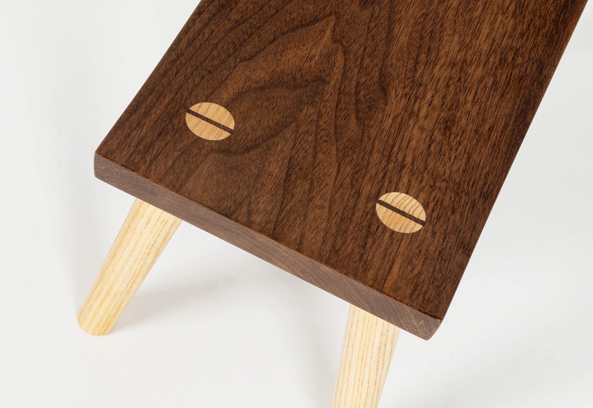 Wooden stool with a dark brown top and light wooden legs on a white background