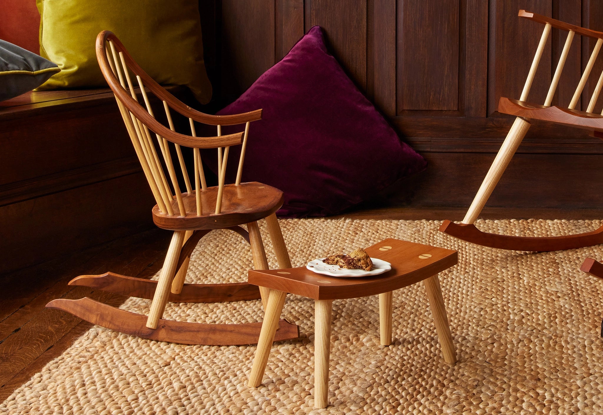 Wooden chair and footstool on a textured floor with pillows in the background