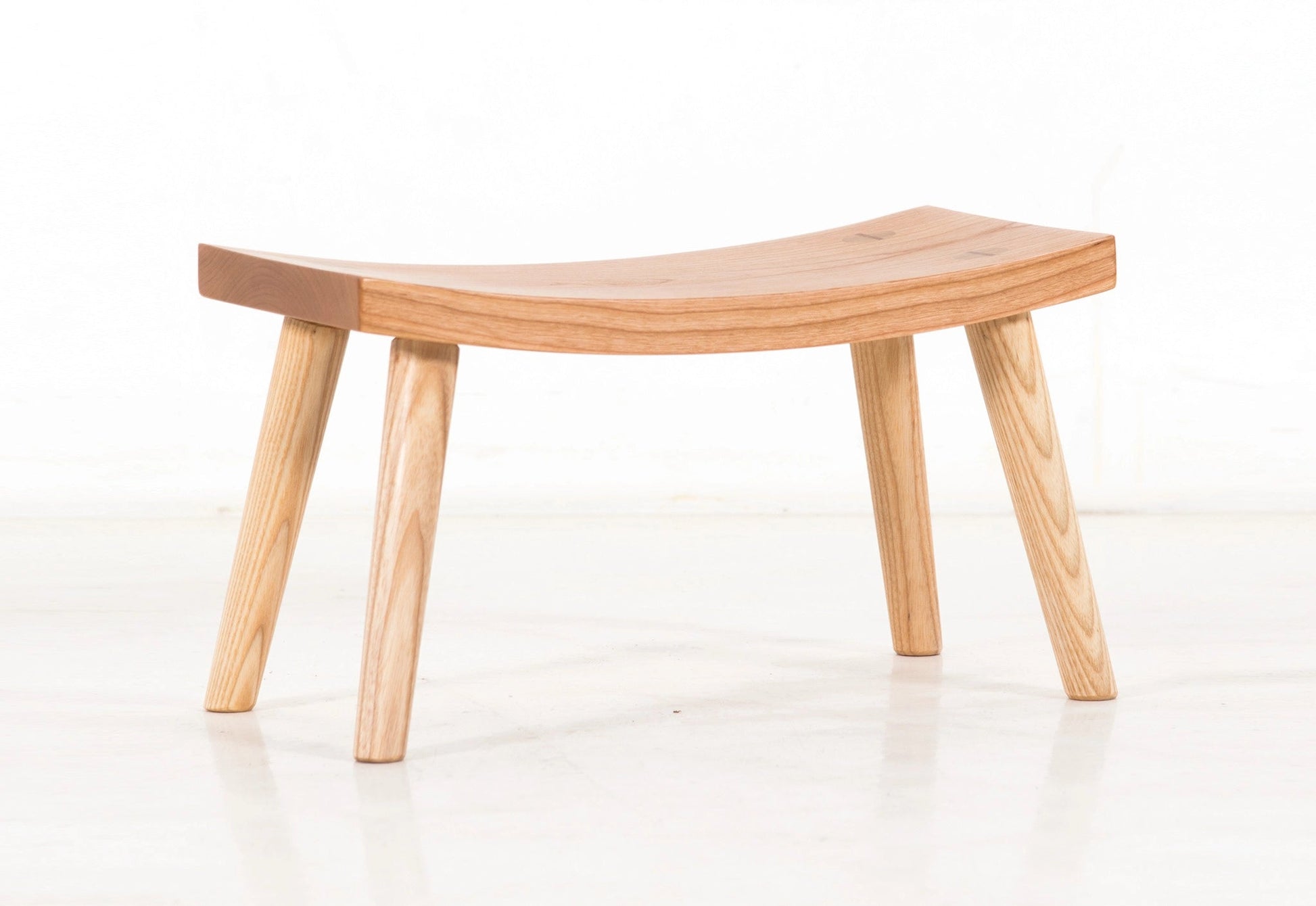 Wooden stool with curved seat and four legs on a white background
