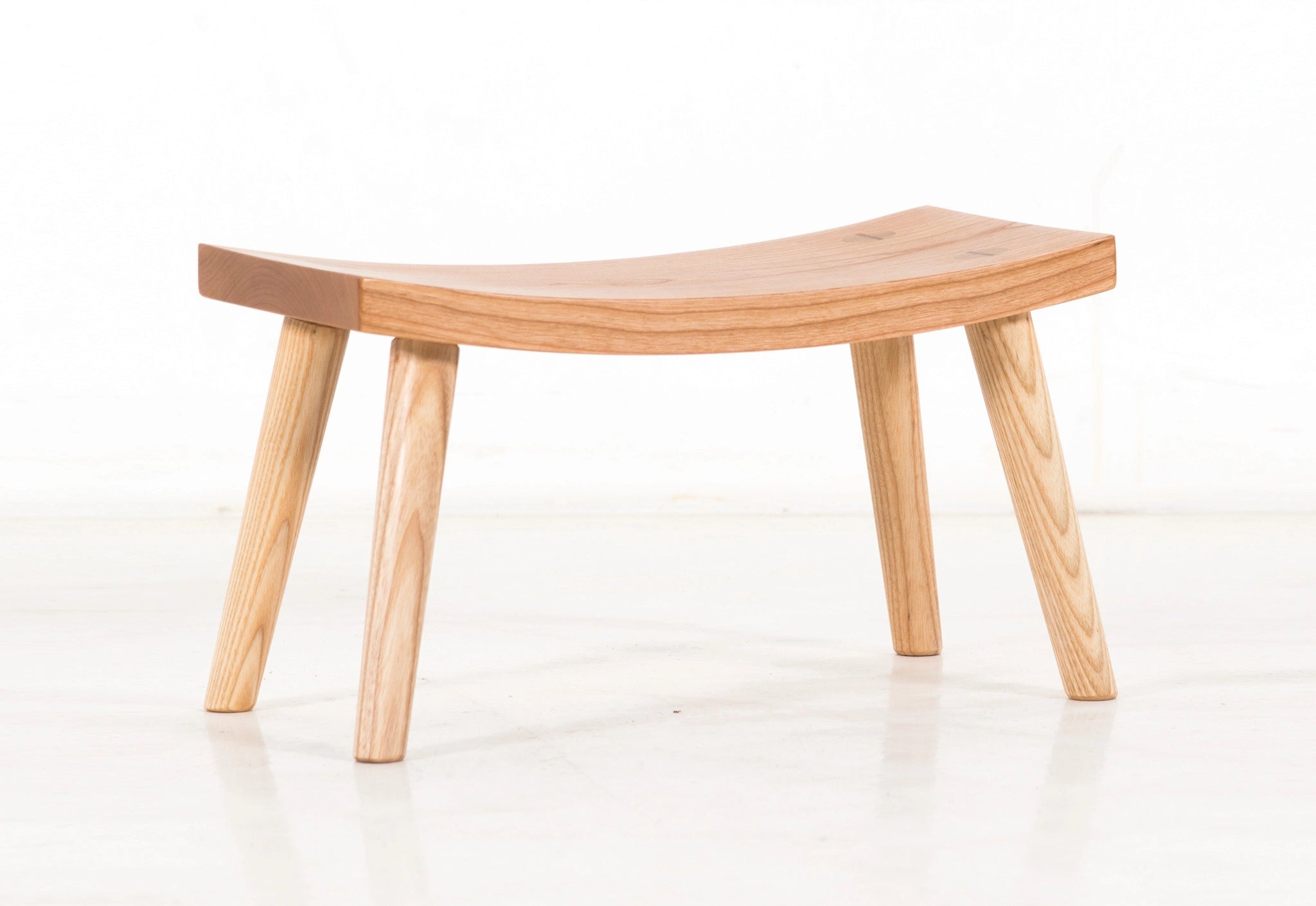 Wooden stool with curved seat and four legs on a white background