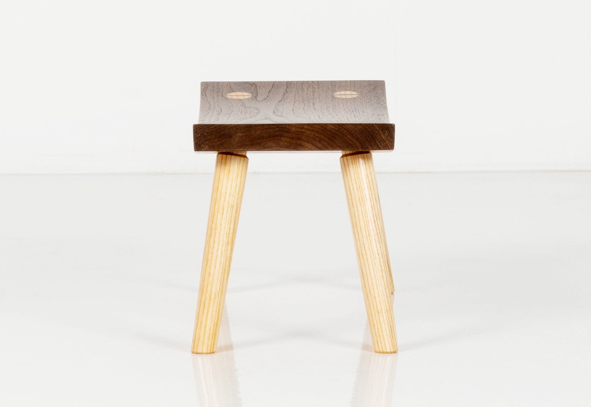 Wooden stool with a dark brown seat and light wood legs on a white background