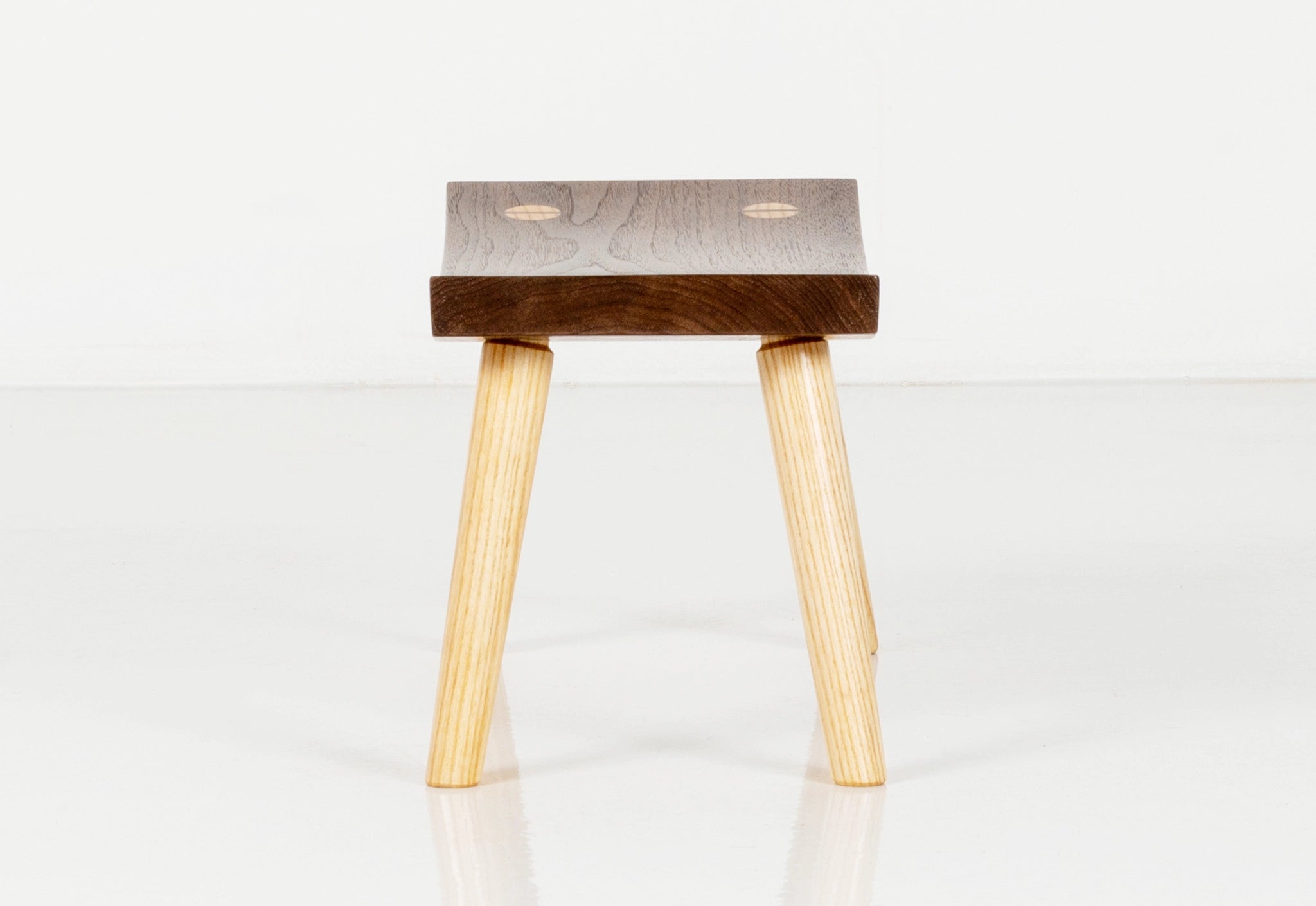Wooden stool with a dark brown seat and light wood legs on a white background