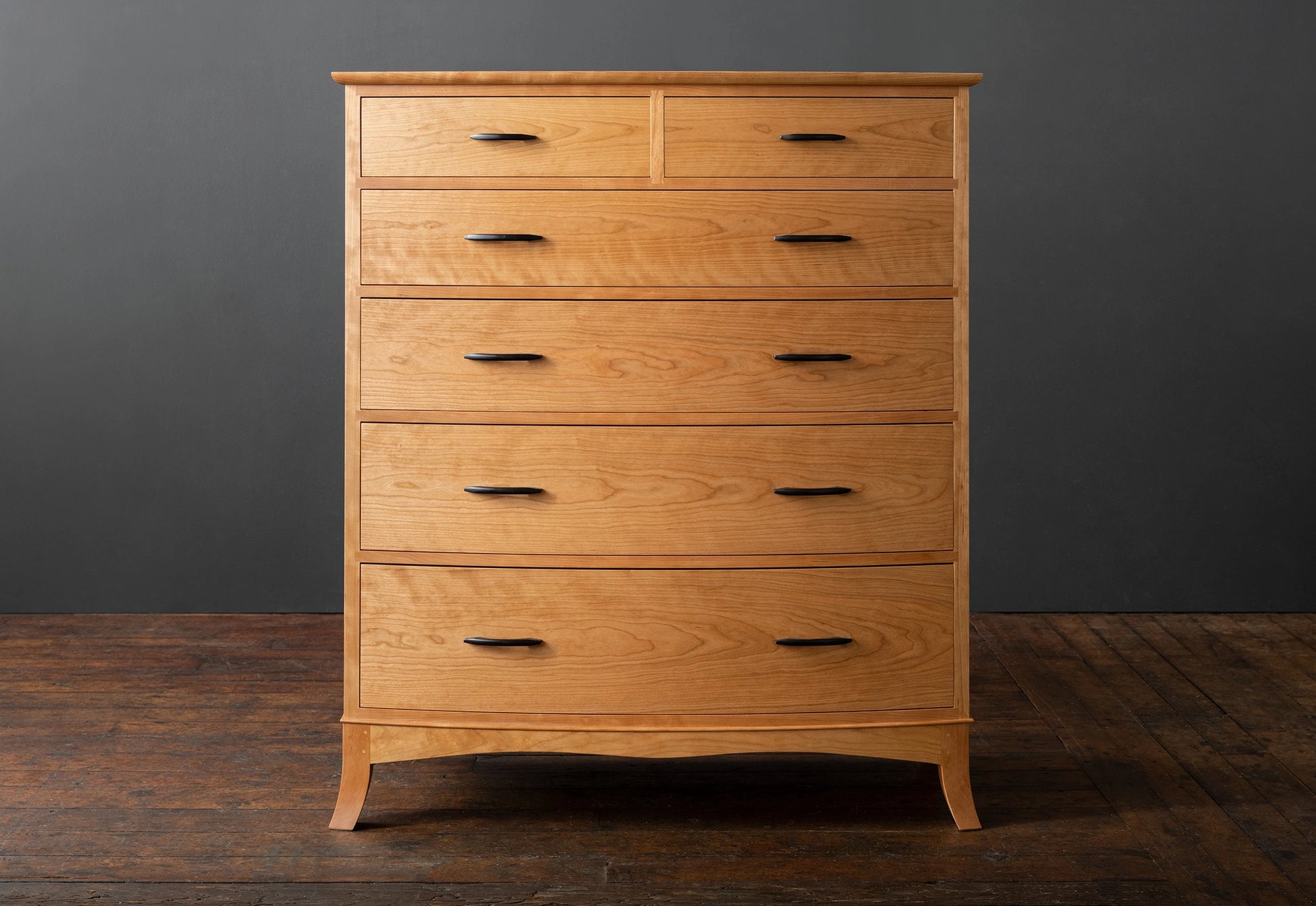 Wooden dresser with multiple drawers against a dark gray wall.