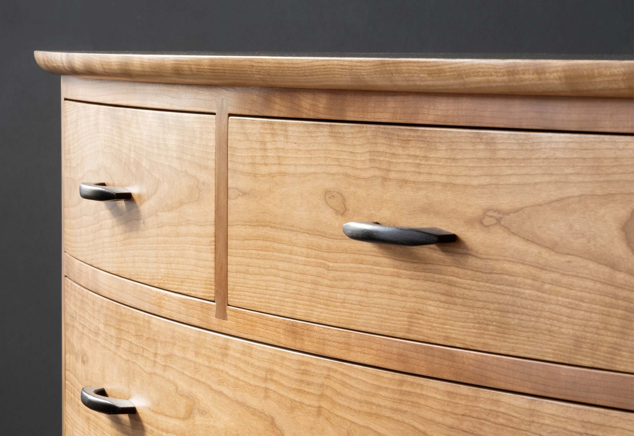 Wooden dresser with three drawers and metal handles on a dark background