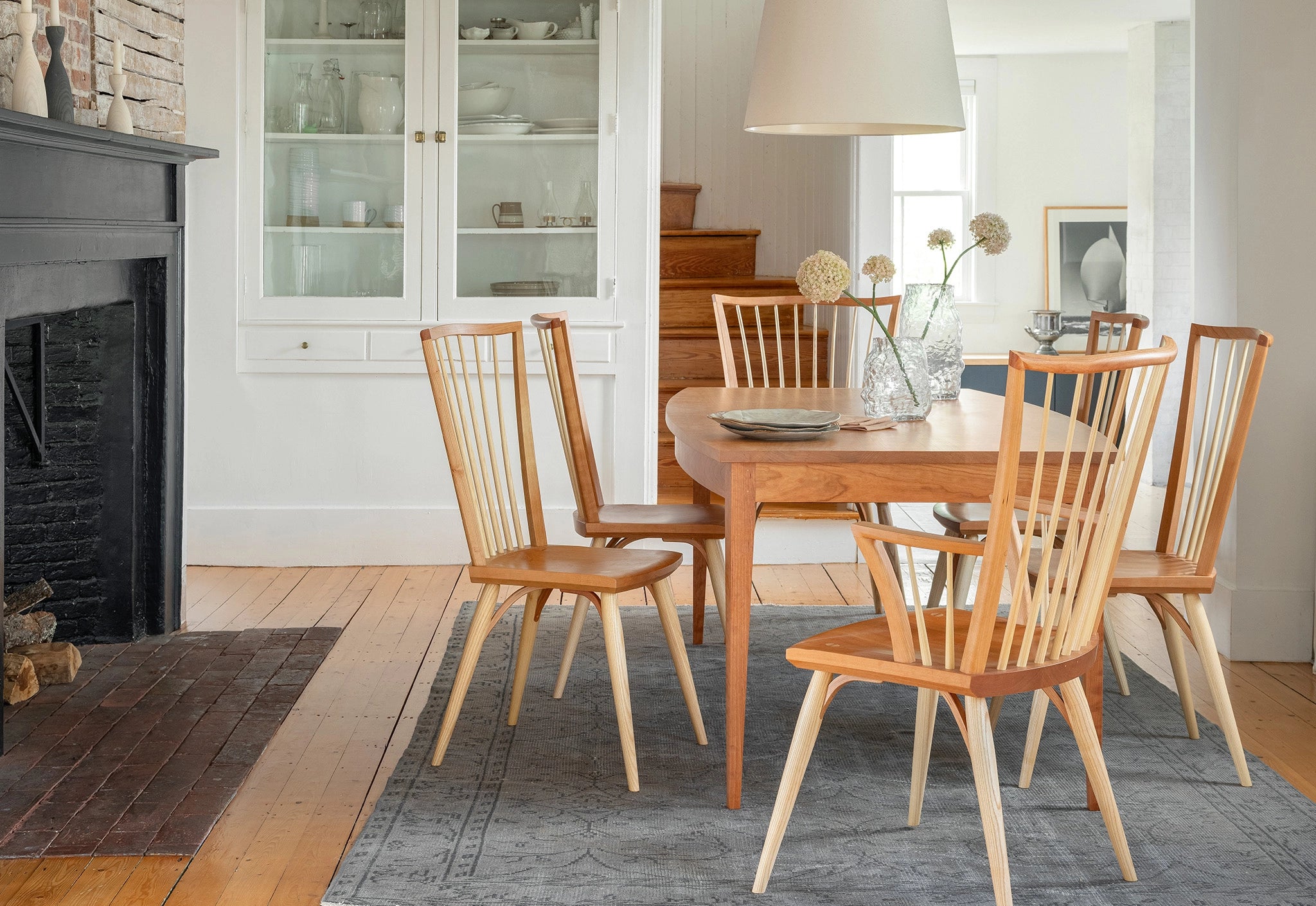 Wooden dining table with chairs in a well-lit room with a fireplace and cabinets.