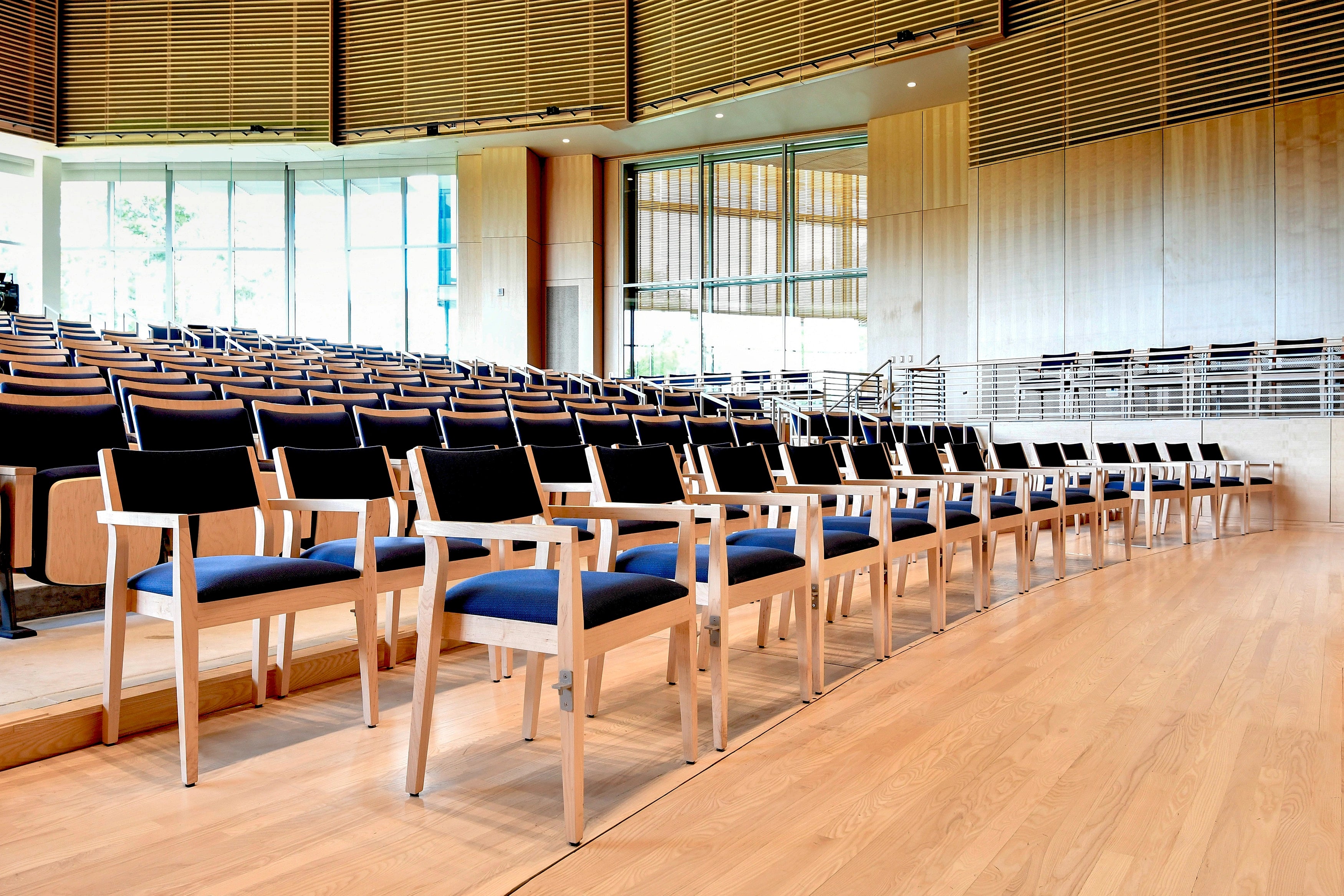 Row of chairs with blue cushions in a large, well-lit room with wooden flooring and large windows.
