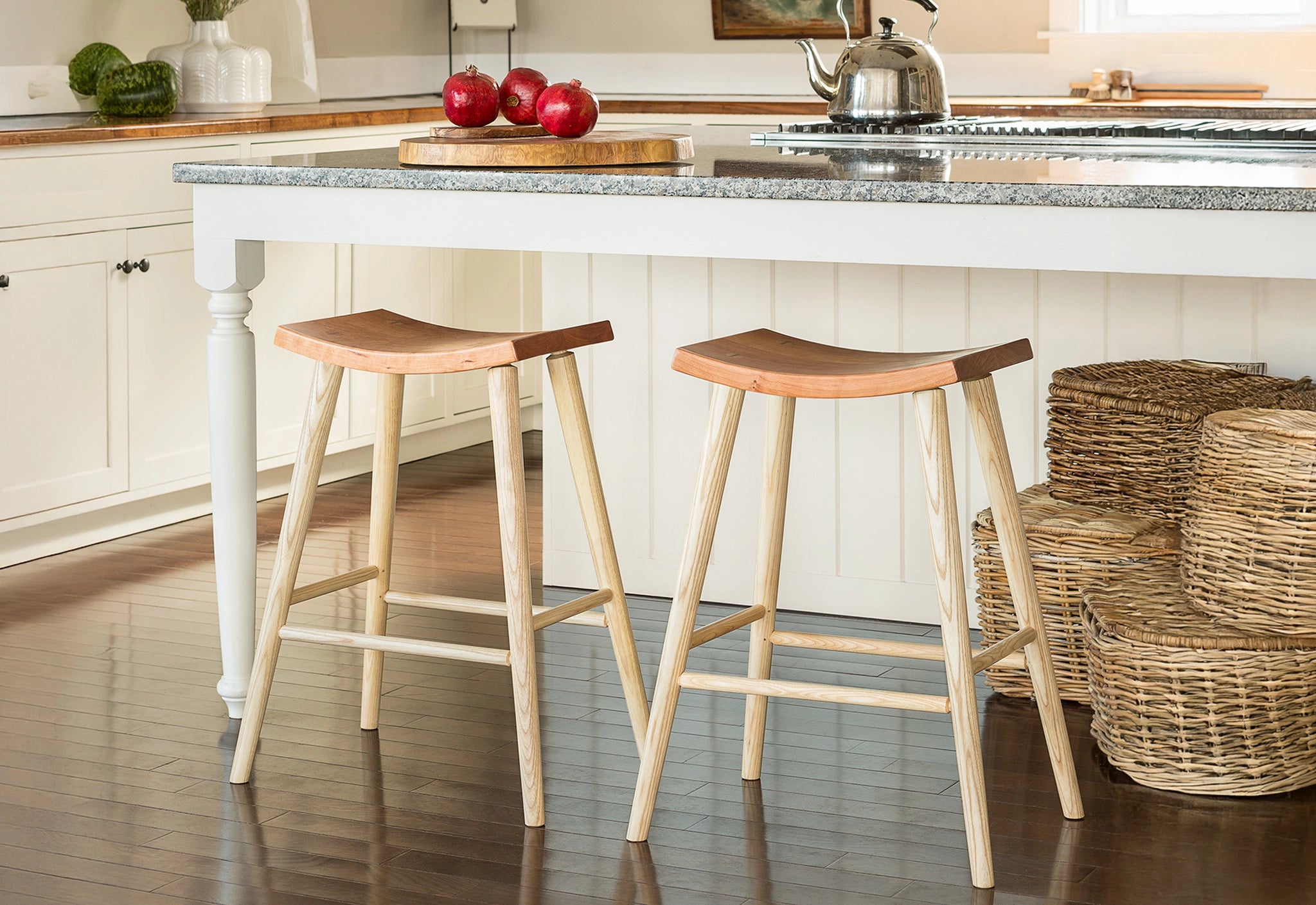 Two wooden stools in a kitchen setting with a white island and wicker baskets.