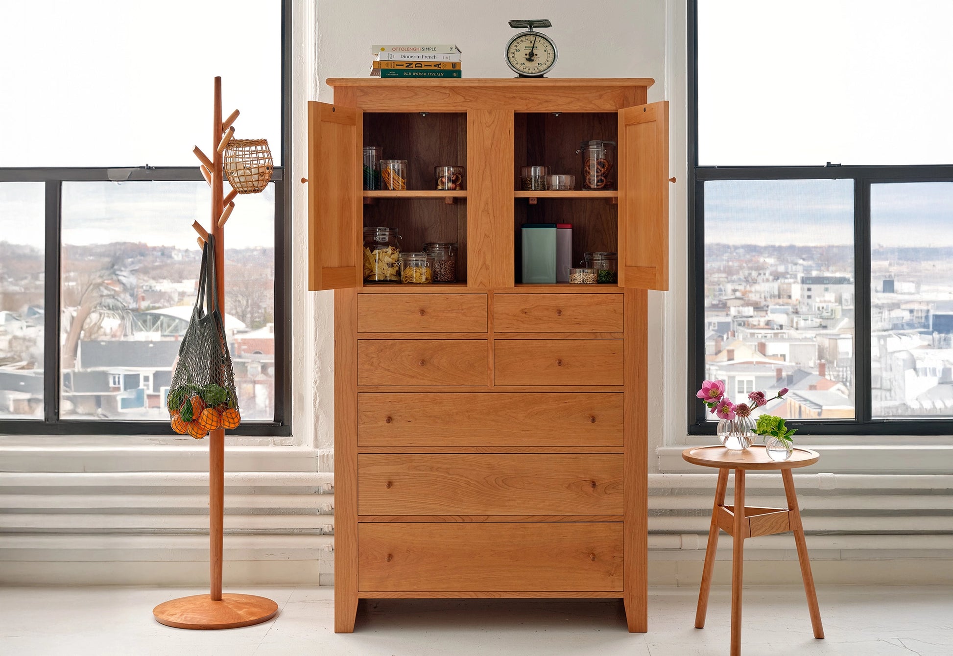 Wooden cabinet with open doors displaying various items in a room with large windows.