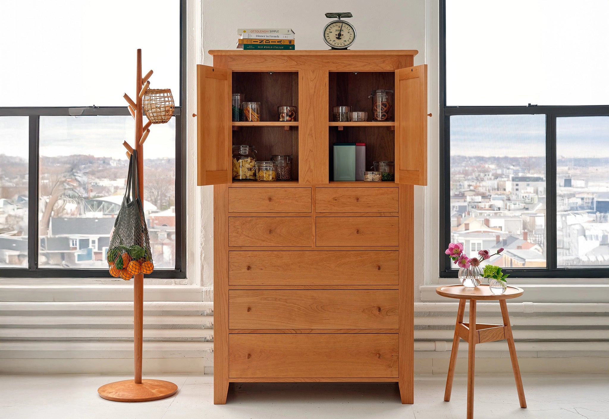 Wooden cabinet with open doors displaying various items in a room with large windows.
