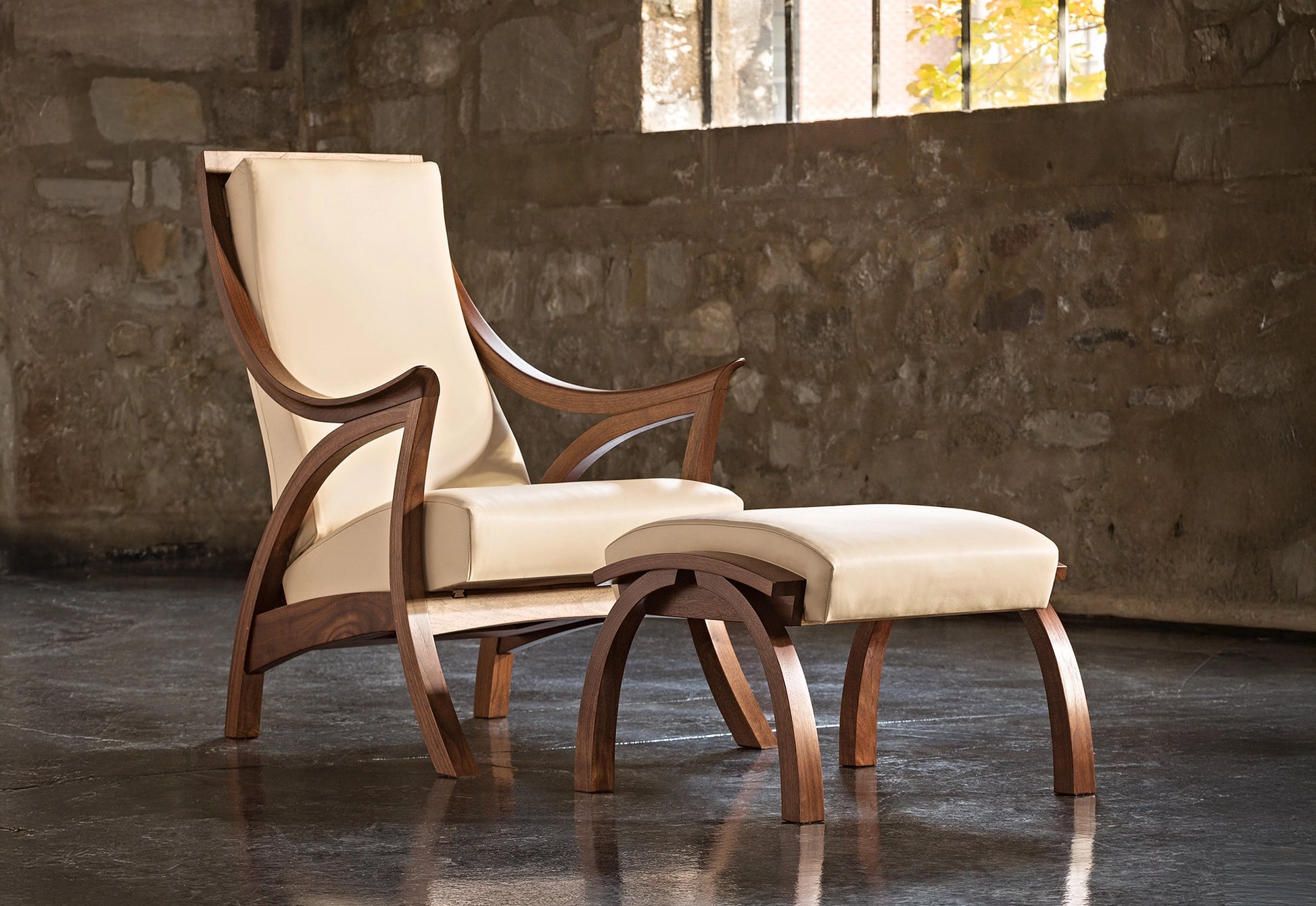 Wooden armchair with cream cushion against a stone wall