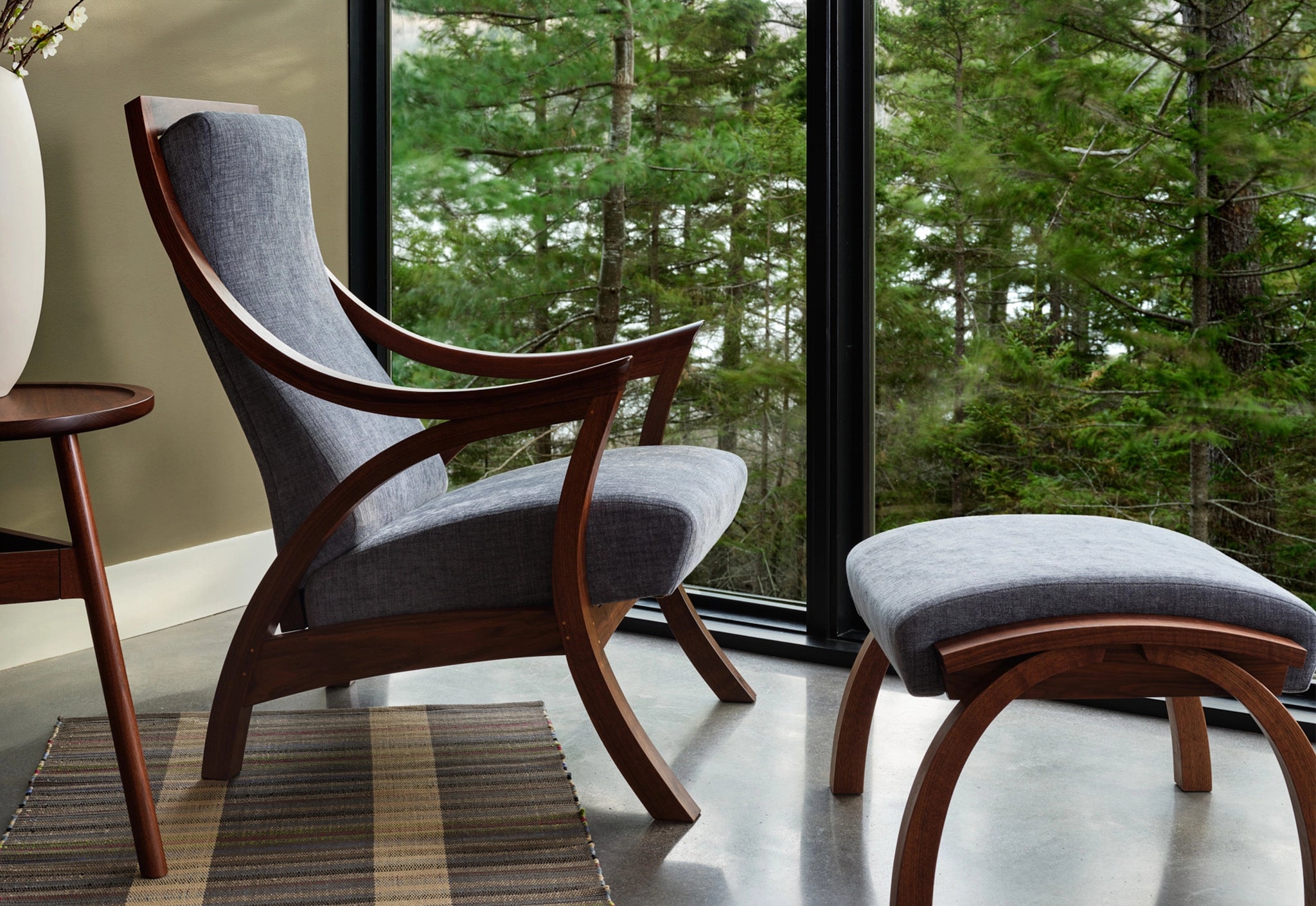 Wooden Lounge Chair and ottoman in a room with large windows showing greenery outside