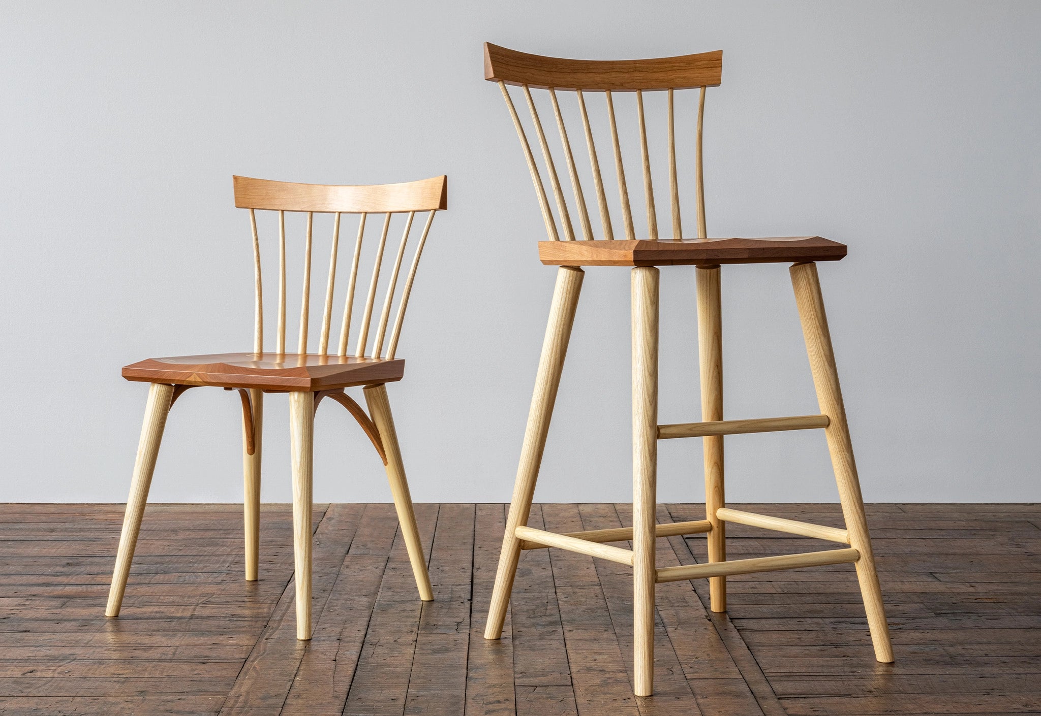 Two wooden chairs on a wooden floor with a gray wall background