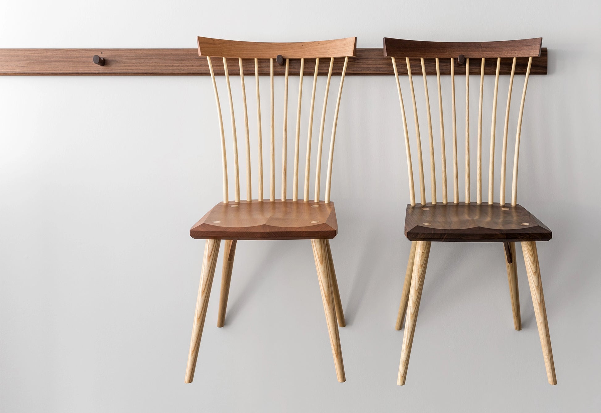 Two wooden chairs with spindled backrests on a plain background
