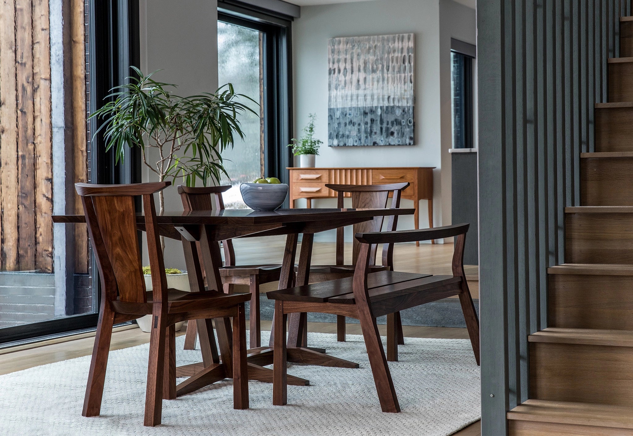 Dining room with wooden table and chairs, plants, and a staircase.