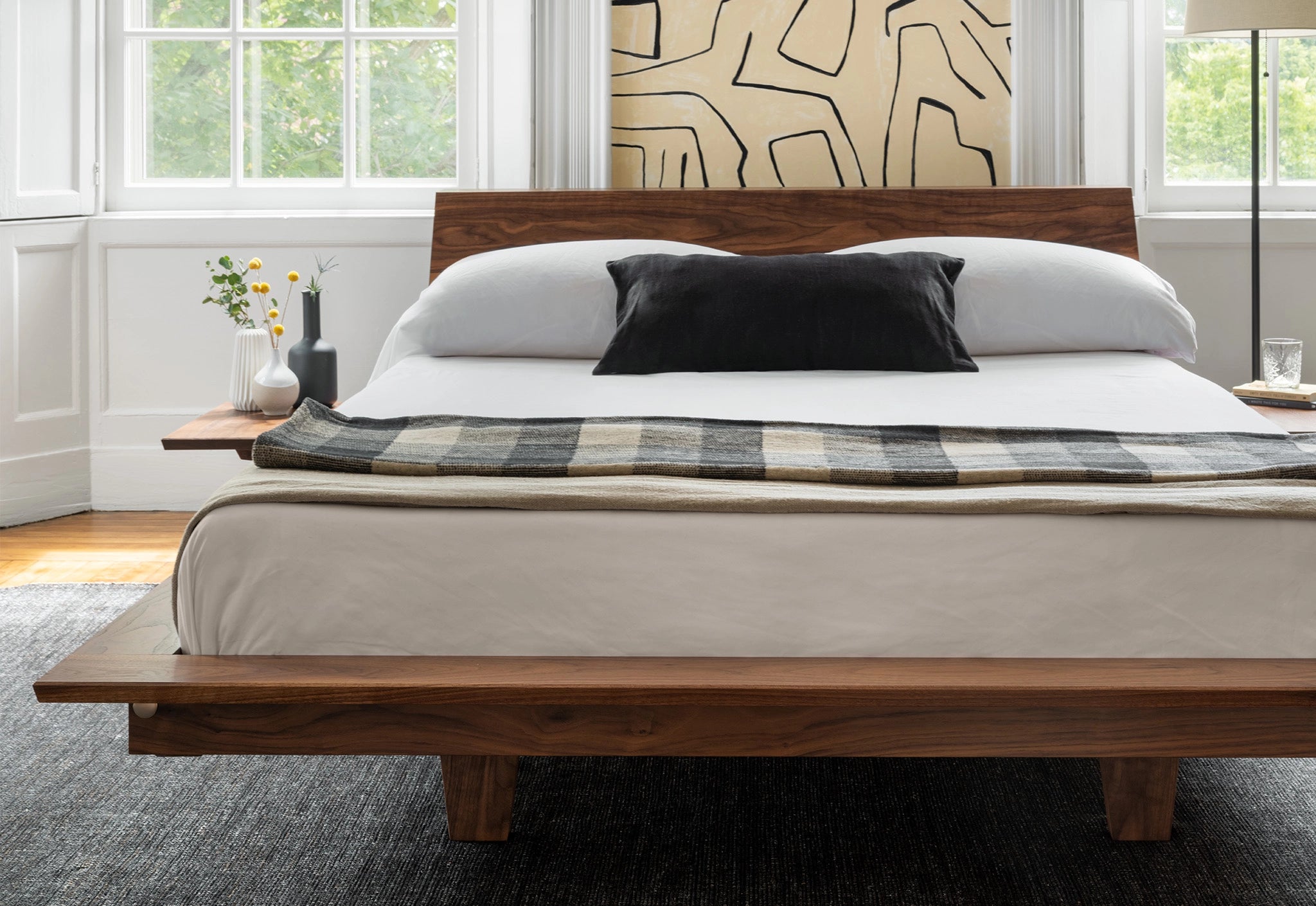 Wooden bed with white bedding and plaid blanket in a bright bedroom.