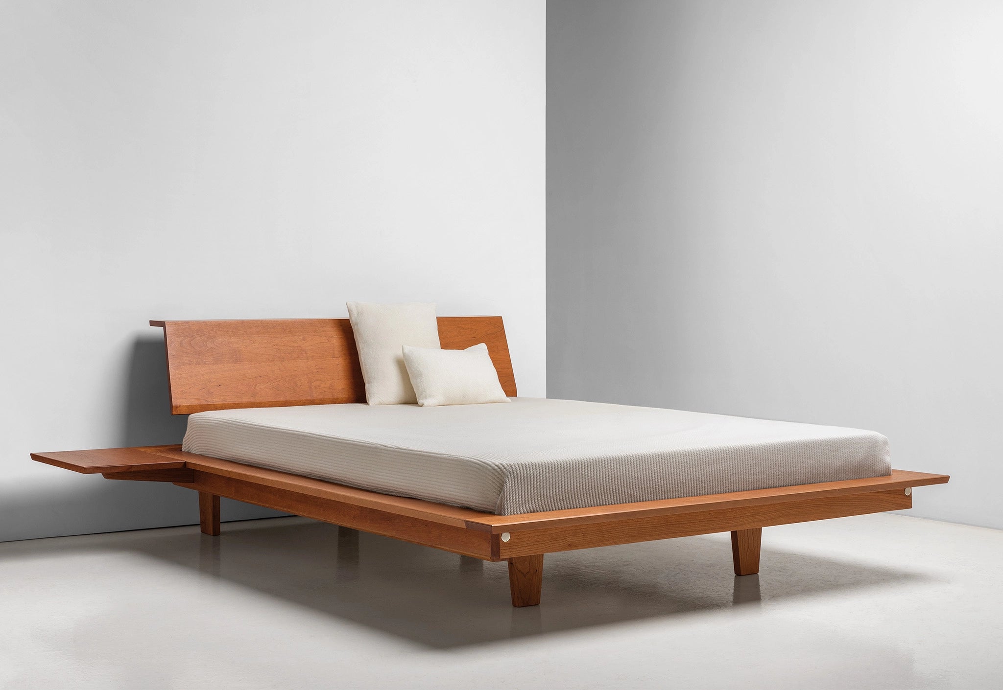 Wooden bed with a white mattress and pillows on a plain background