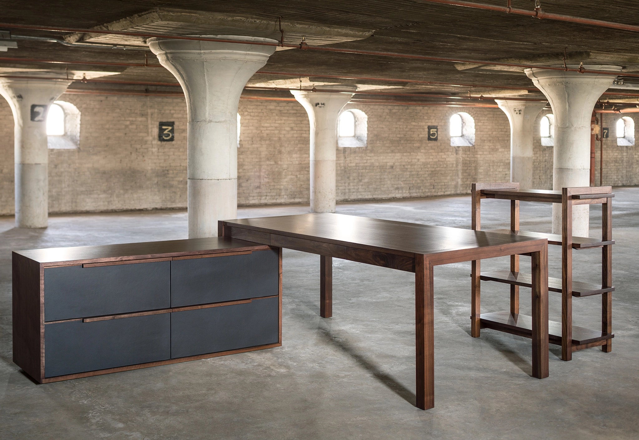 Modern office furniture including a desk and storage unit in an industrial-style room with concrete floors and exposed beams.