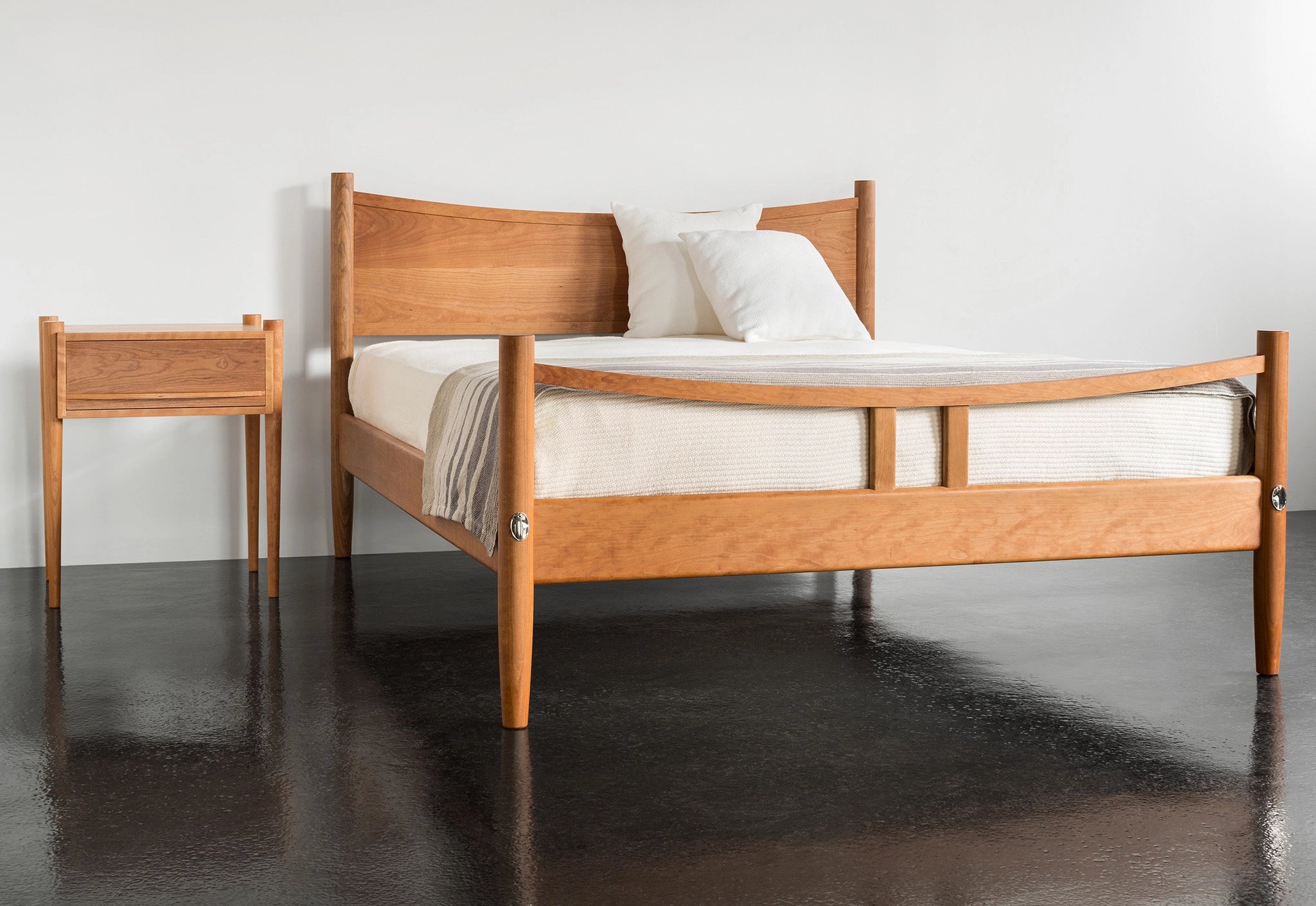 Wooden bed with white bedding and pillows in a minimalistic room.
