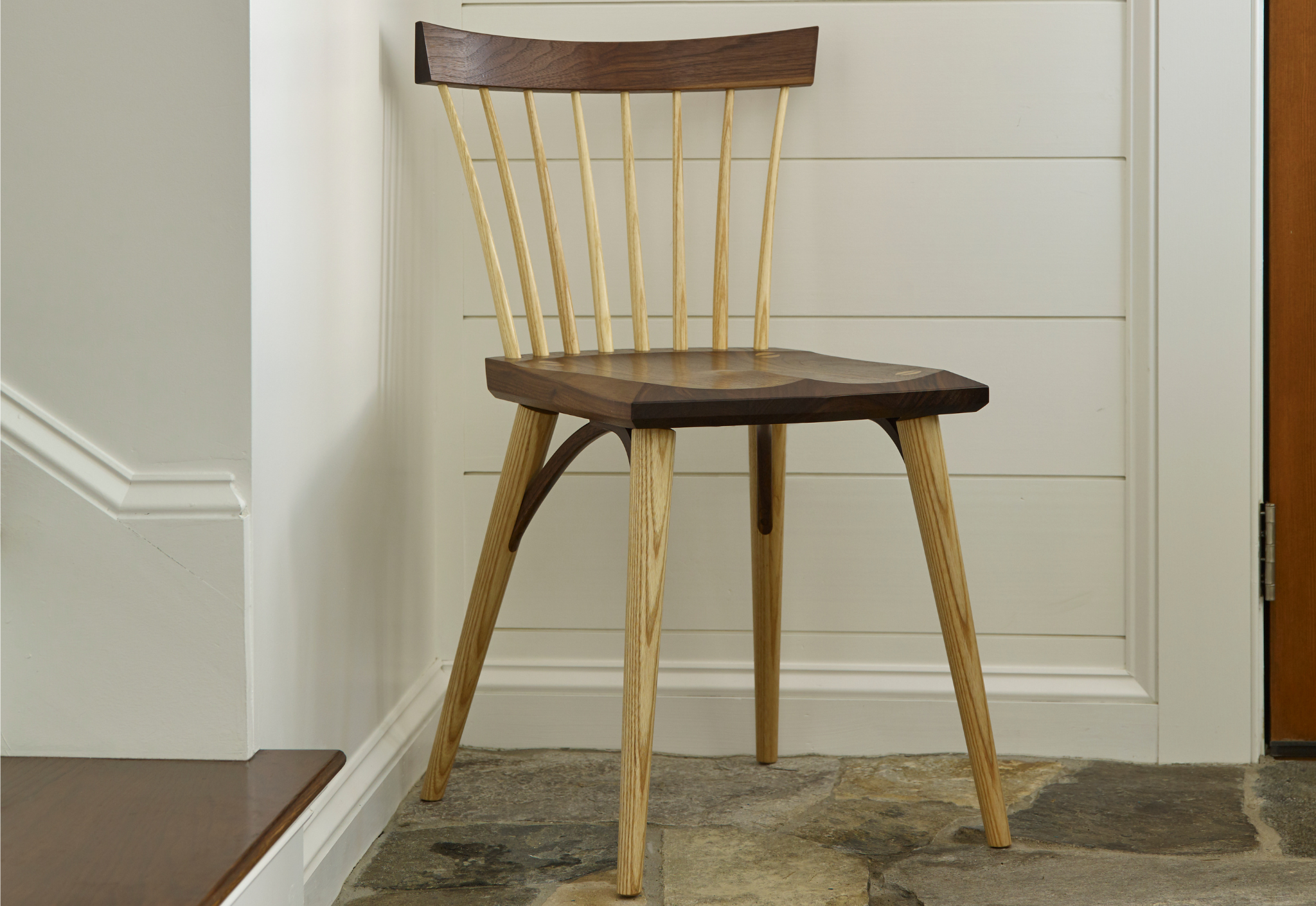 Wooden chair with a dark wooden seat against a white wall.