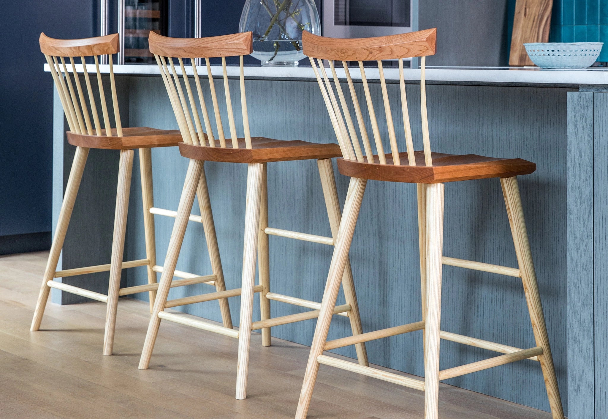 Three wooden bar stools with white legs against a blue wall.
