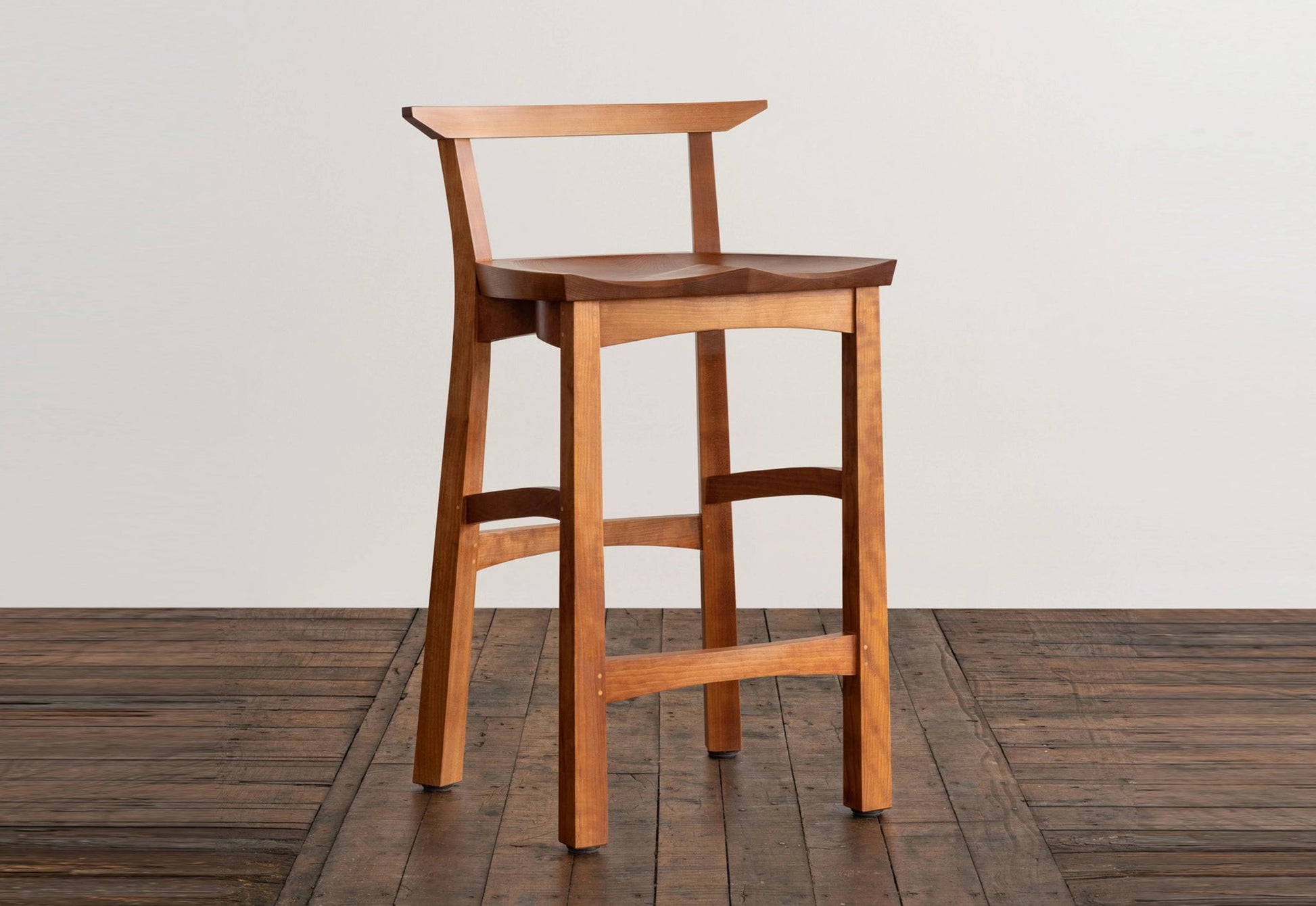 Wooden bar stool on a wooden floor with a white wall background